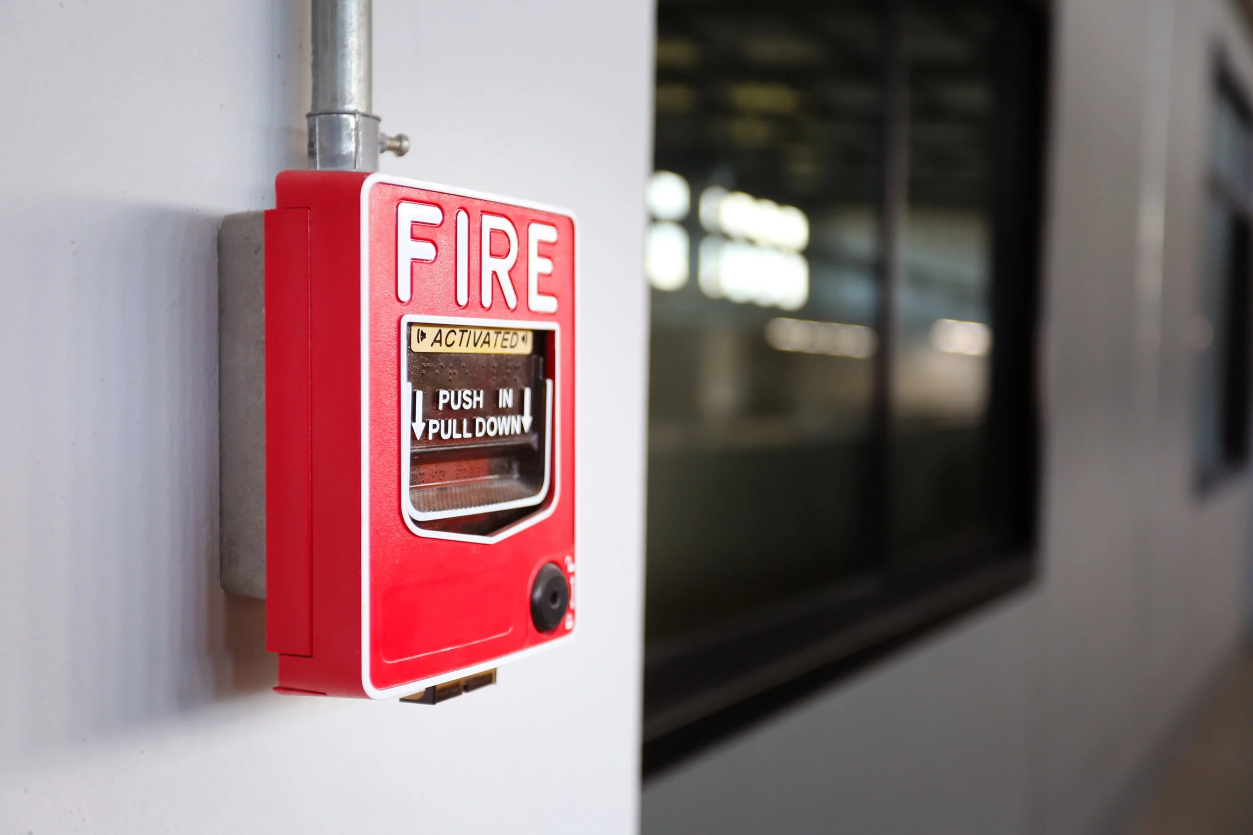 Red fire alarm with the label 'ACTIVATED' mounted on a white wall in an indoor space.