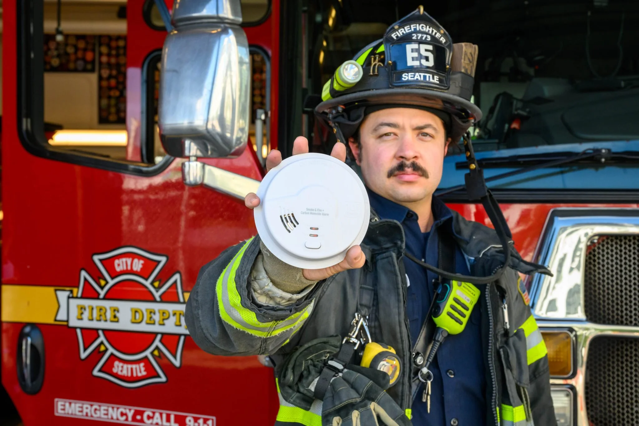 Firefighter holding a smoke detector in front of a fire truck.