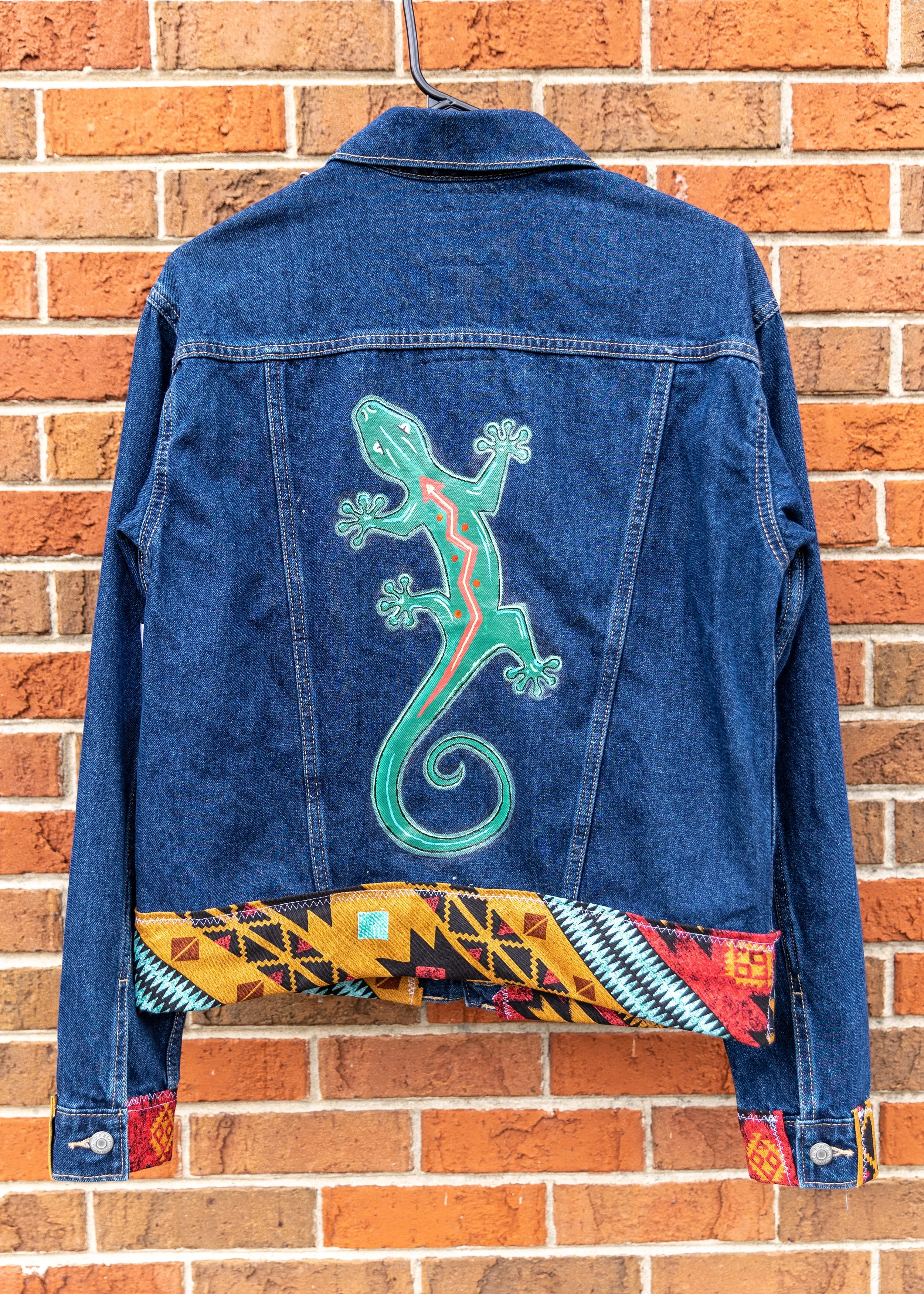 Denim jacket with neon gecko design hanging on a brick wall
