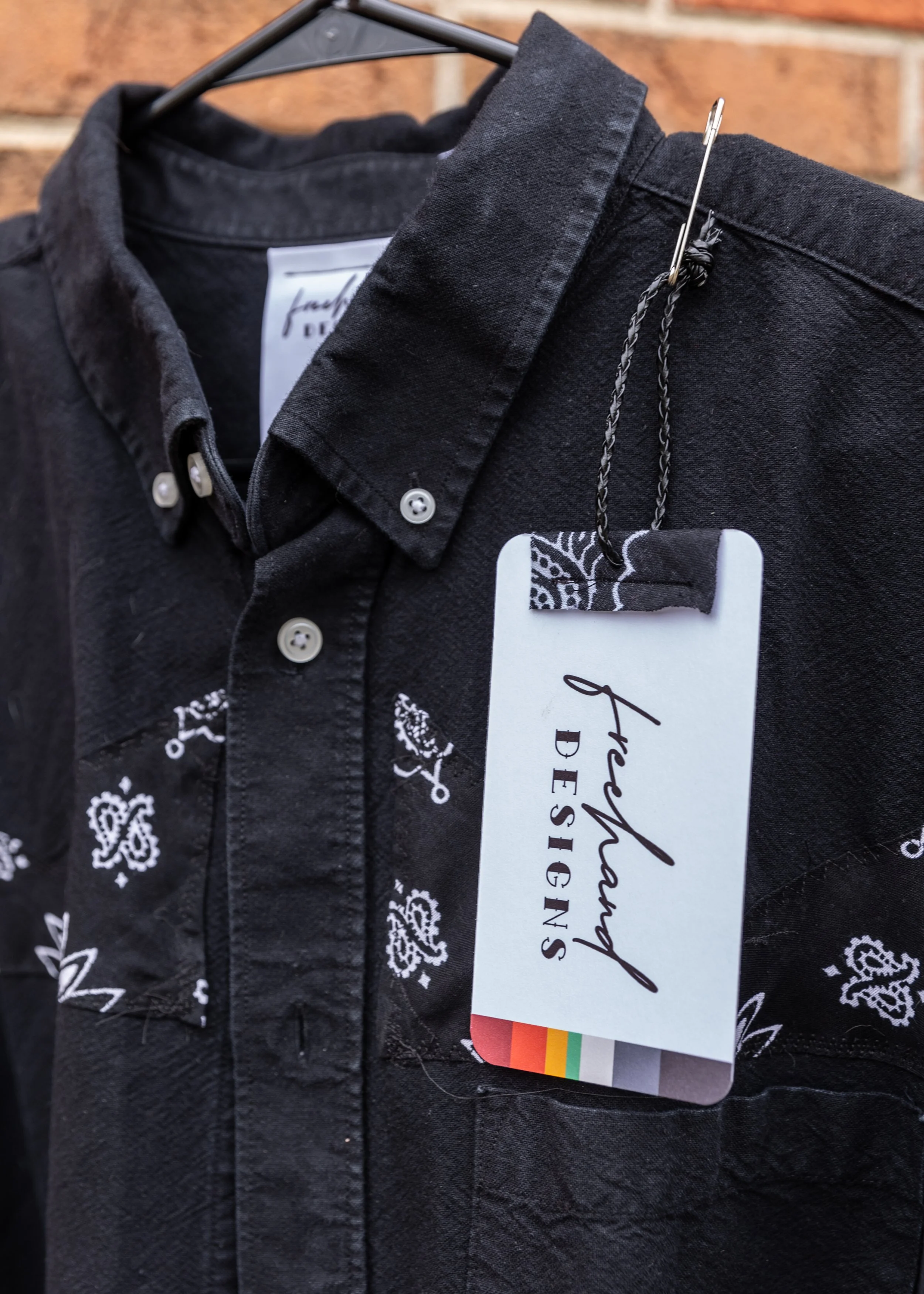 Close-up of black pants on a hanger with a white tag attached, showing a black and white printed fabric detail and white paisley patterns.