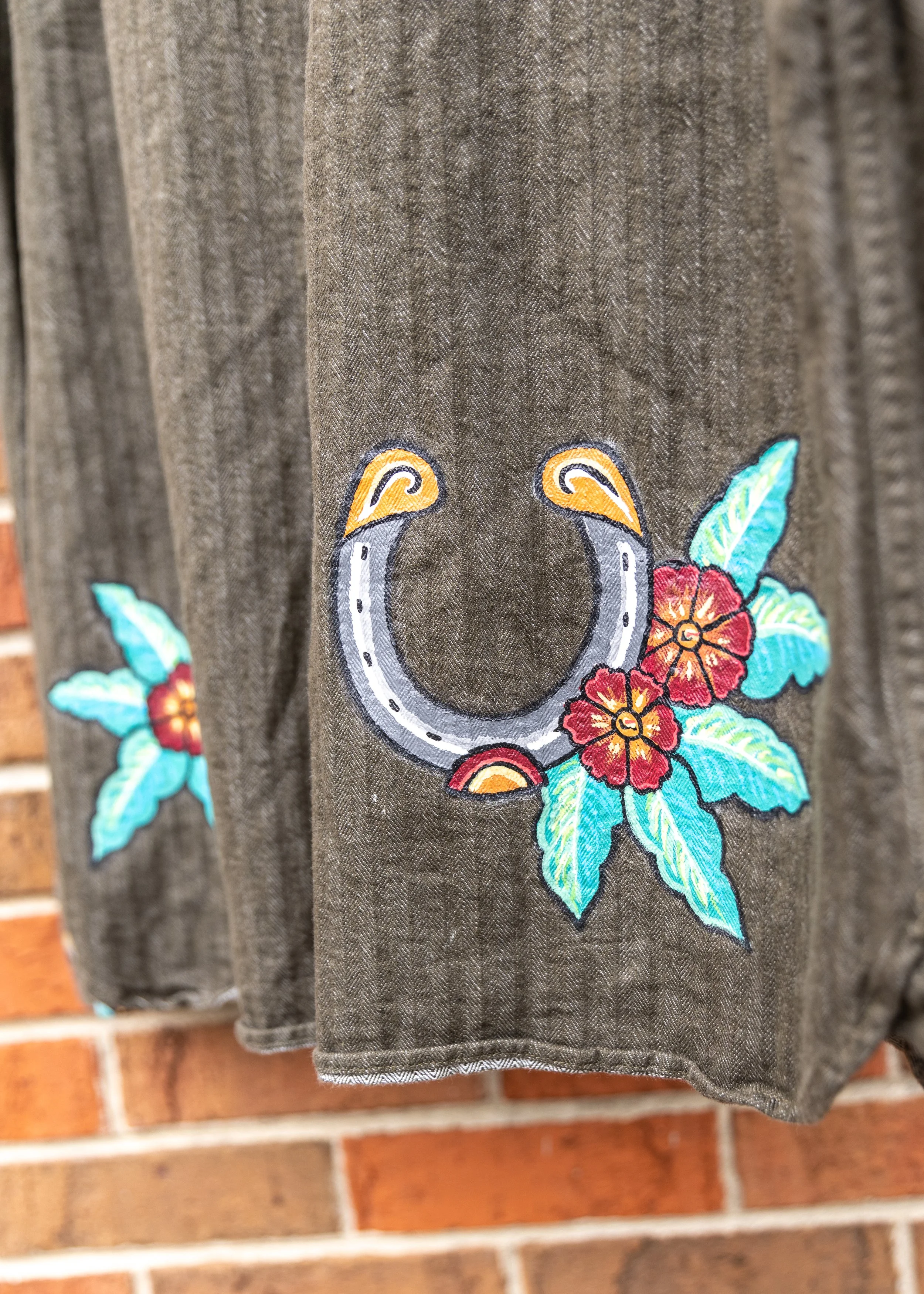 Close-up of embroidered horseshoe with orange flowers and teal leaves on a dark fabric background.