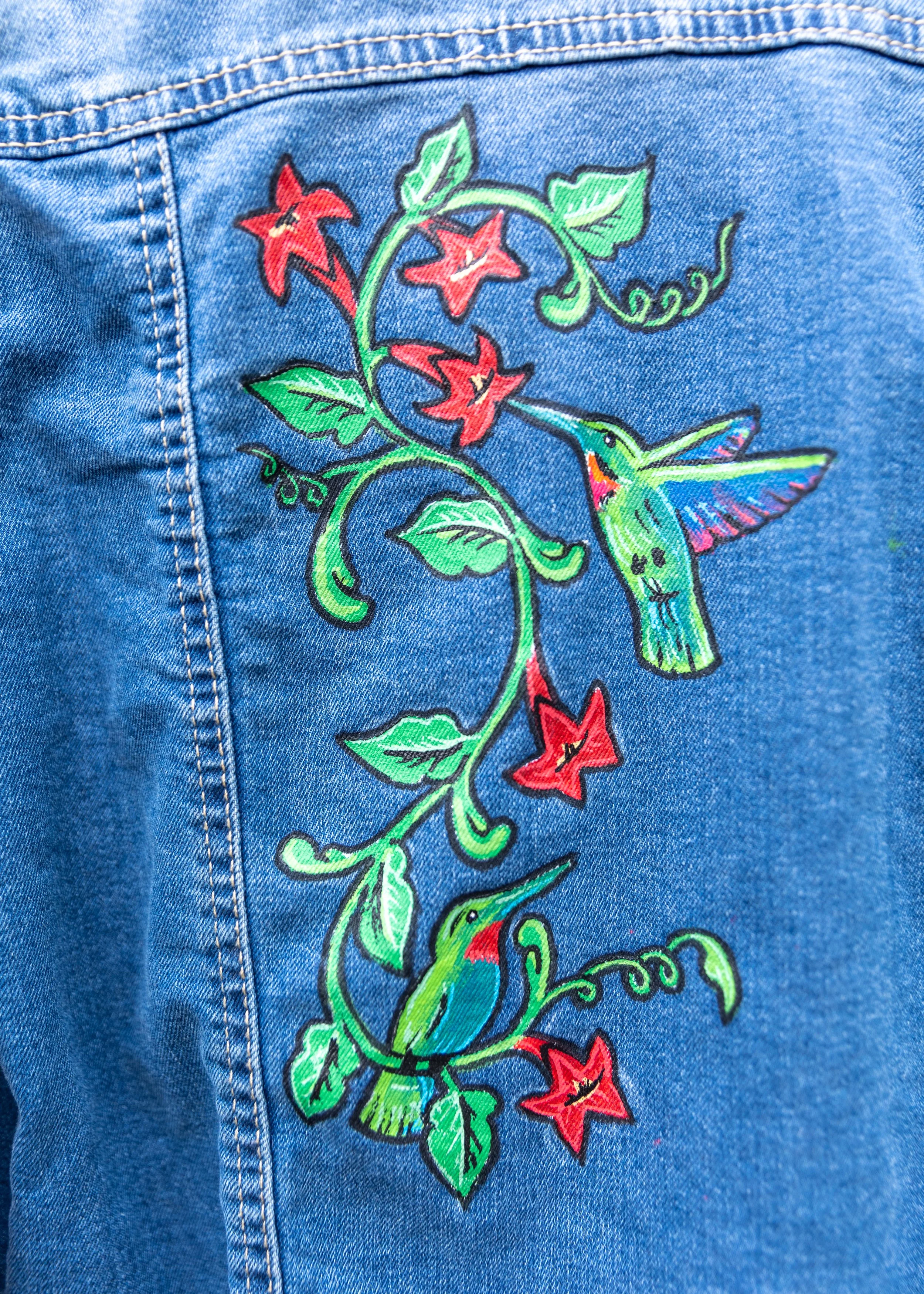 Close-up of denim fabric with colorful embroidered floral and hummingbird design.
