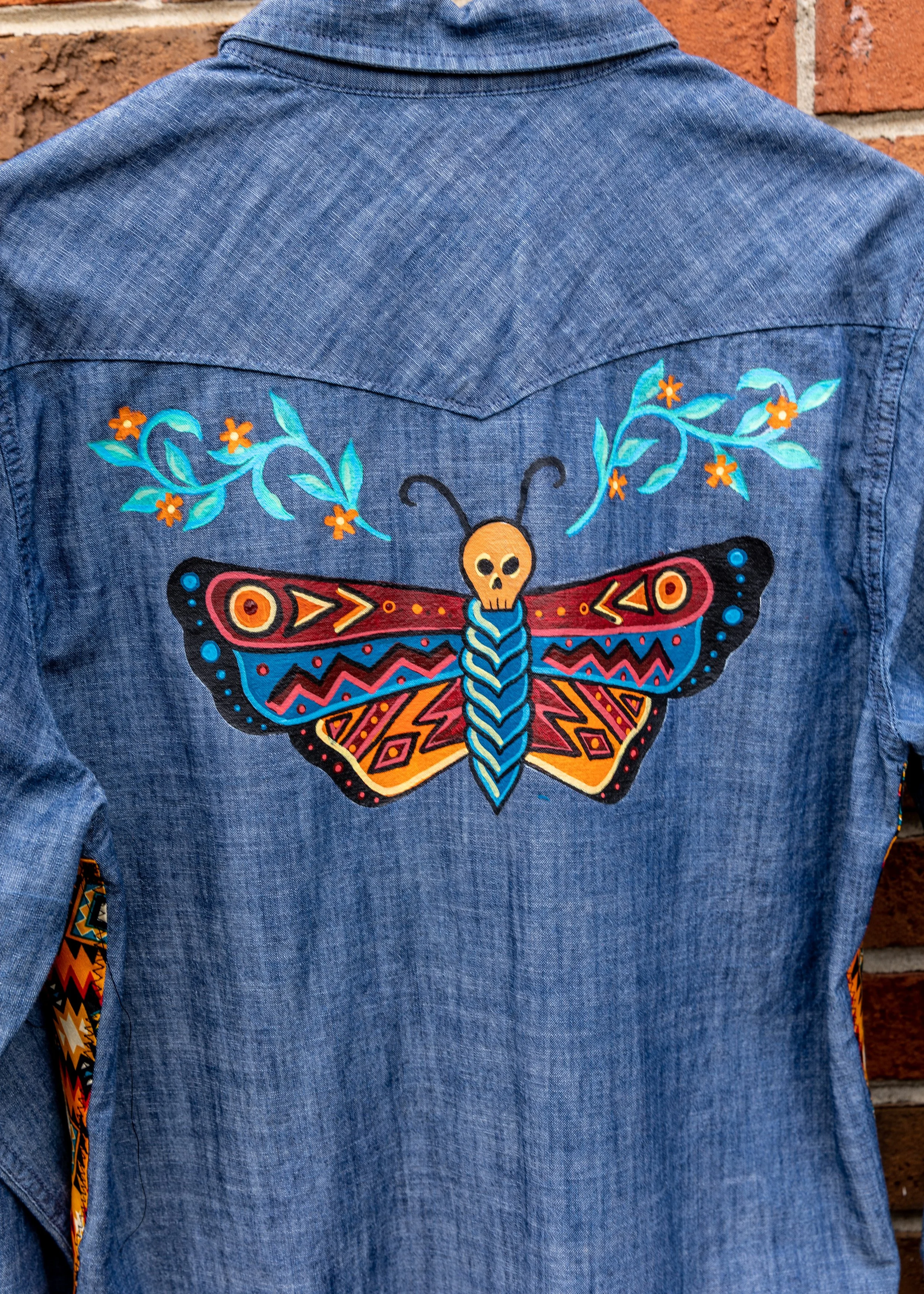 Back of a denim jacket with colorful embroidered butterfly and floral design.