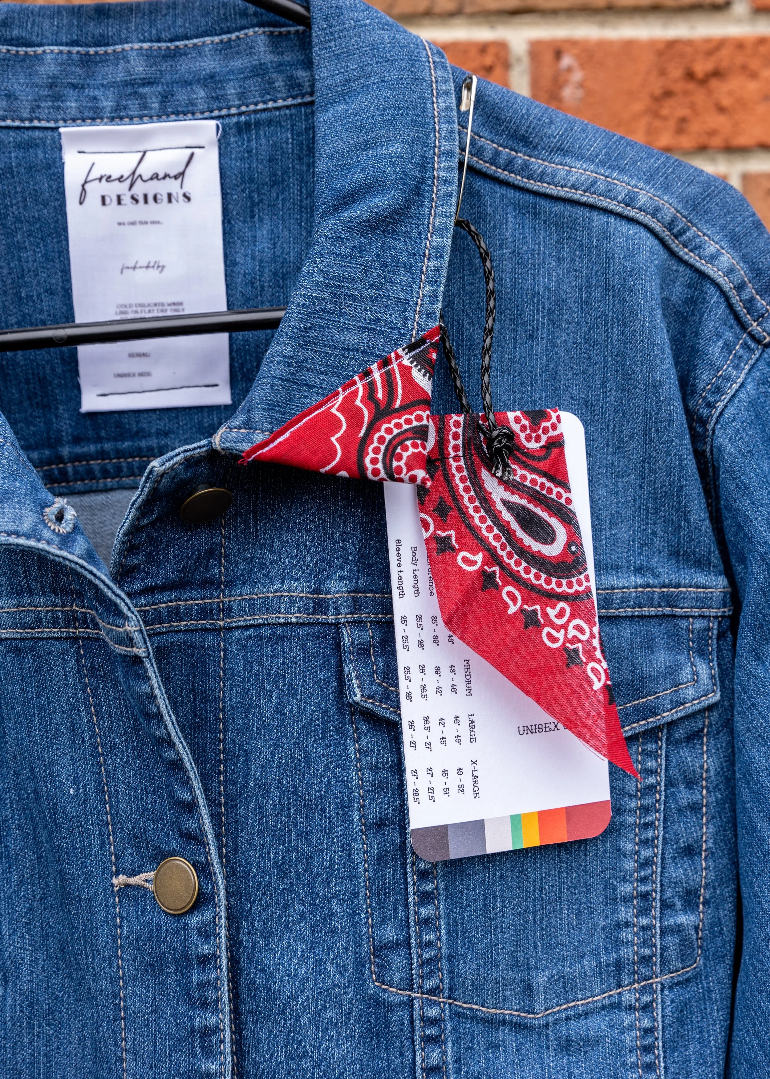 Close-up of a blue denim jacket with a red and white patterned bandana tucked into the chest pocket and a clothing tag hanging from the pocket.