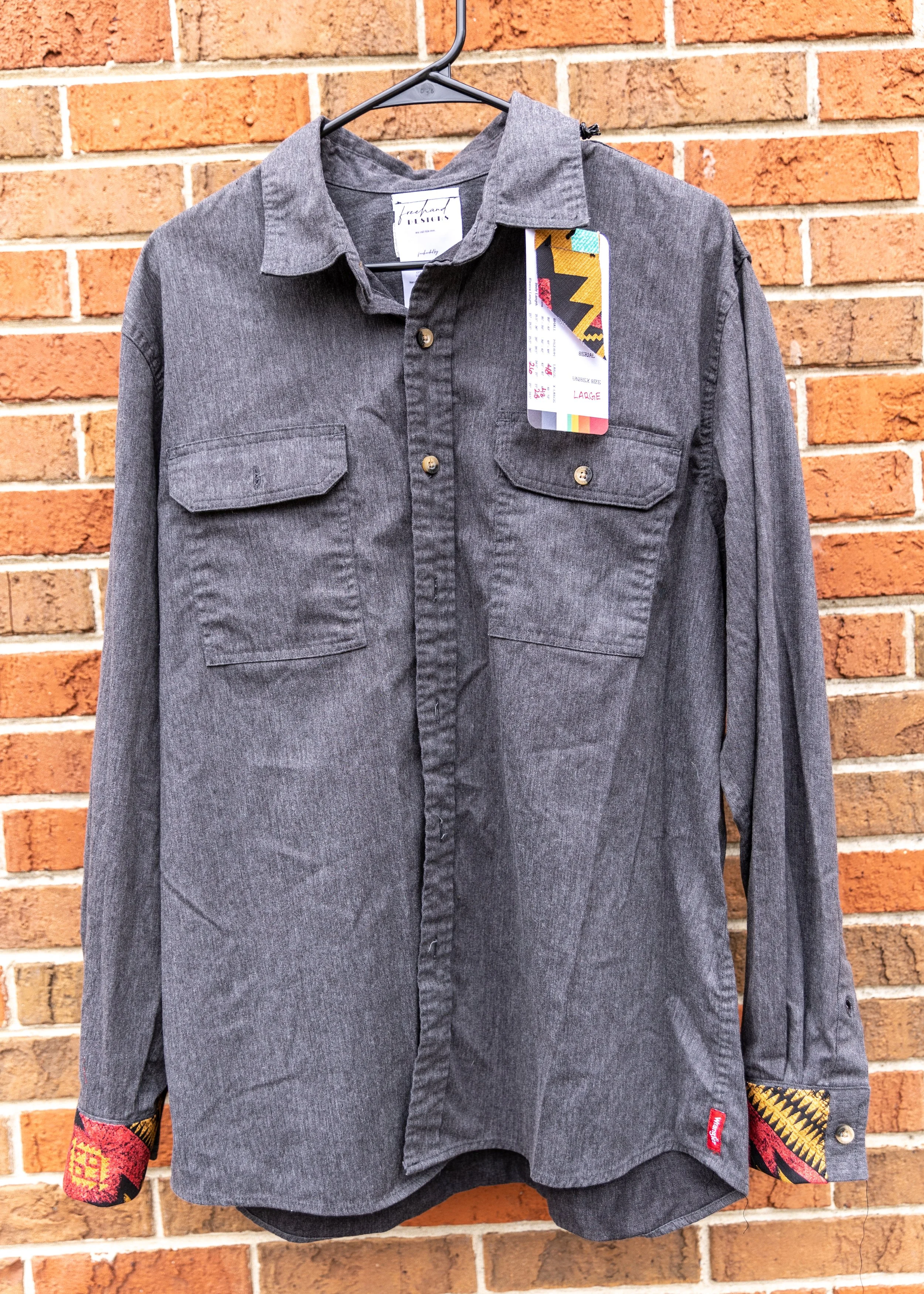 Gray button-up shirt with patterned cuffs hanging on a black hanger against a brick wall.