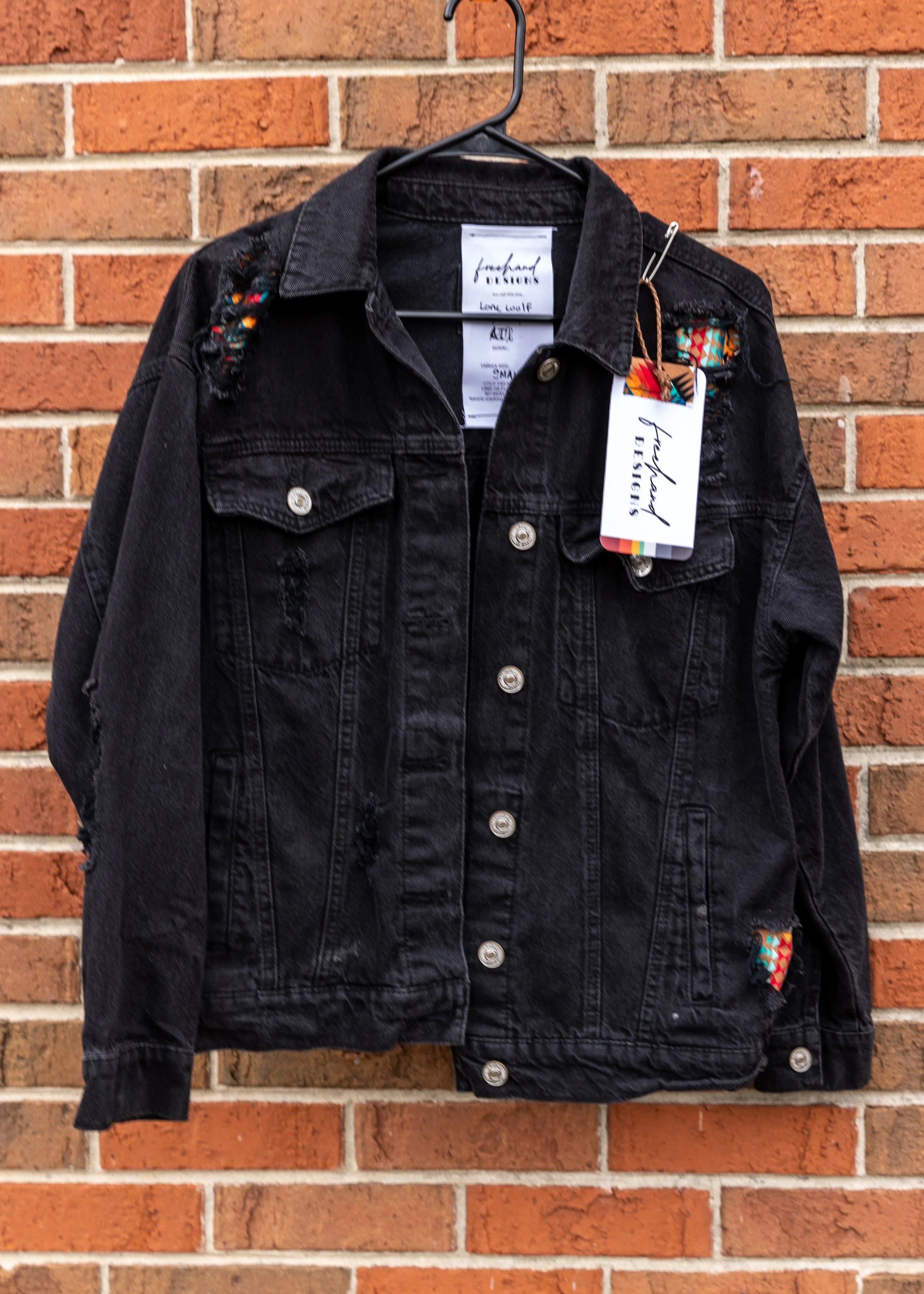 Black denim jacket hanging on a black hanger against a brick wall.