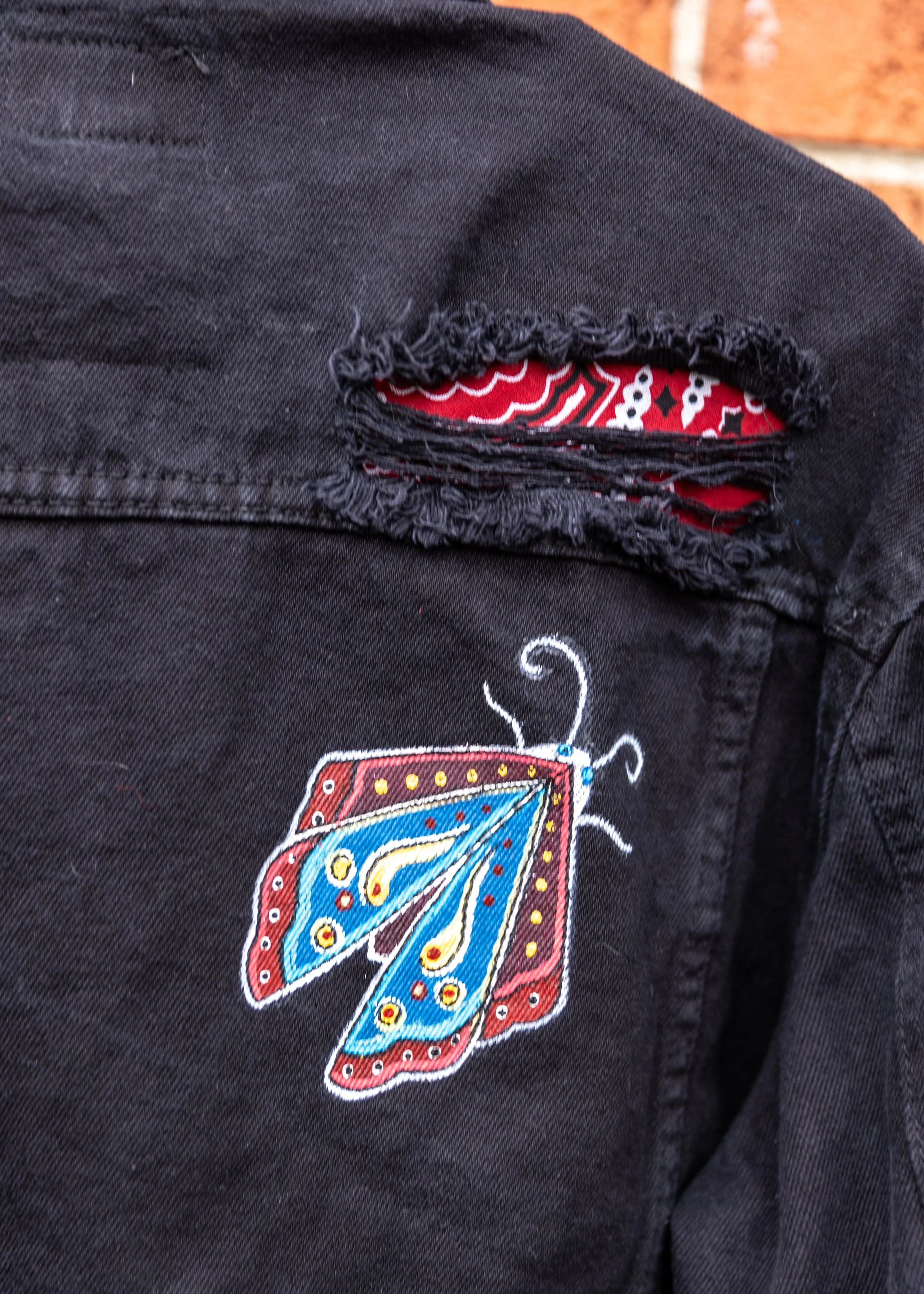 Close-up of black fabric with a tear revealing a colorful, patterned fabric underneath.