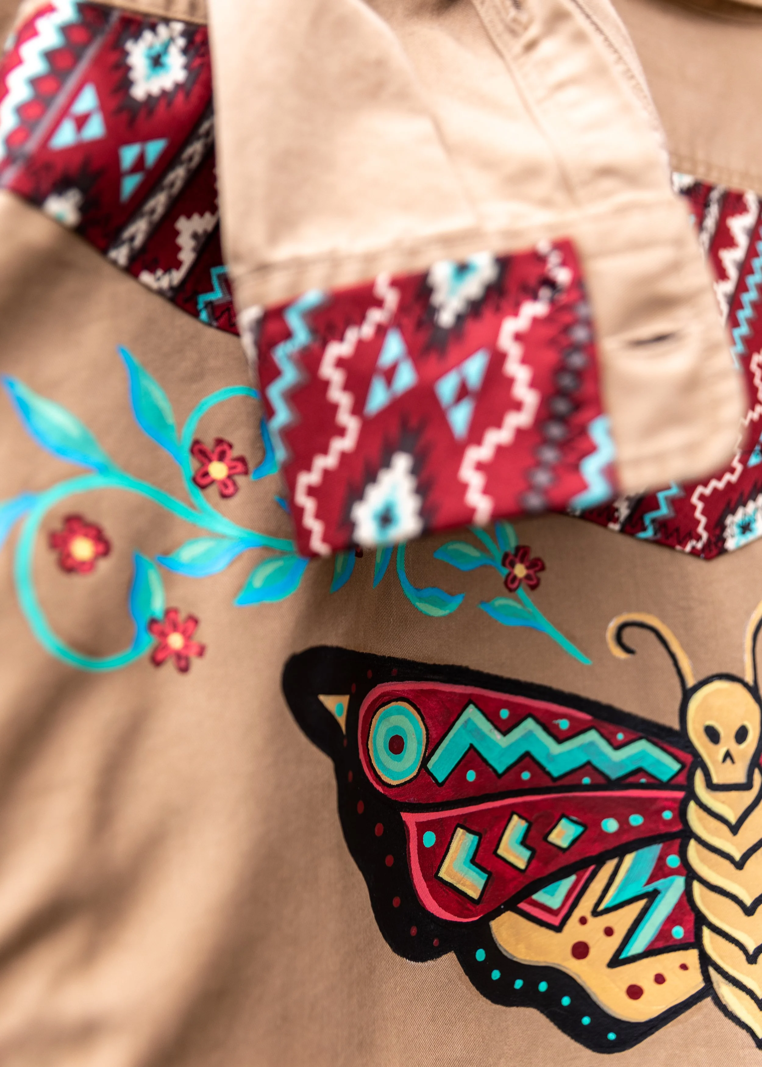 Close-up of fabric with colorful graphic design and embroidered geometric patterns, including red, blue, black, and yellow elements, on a tan background.