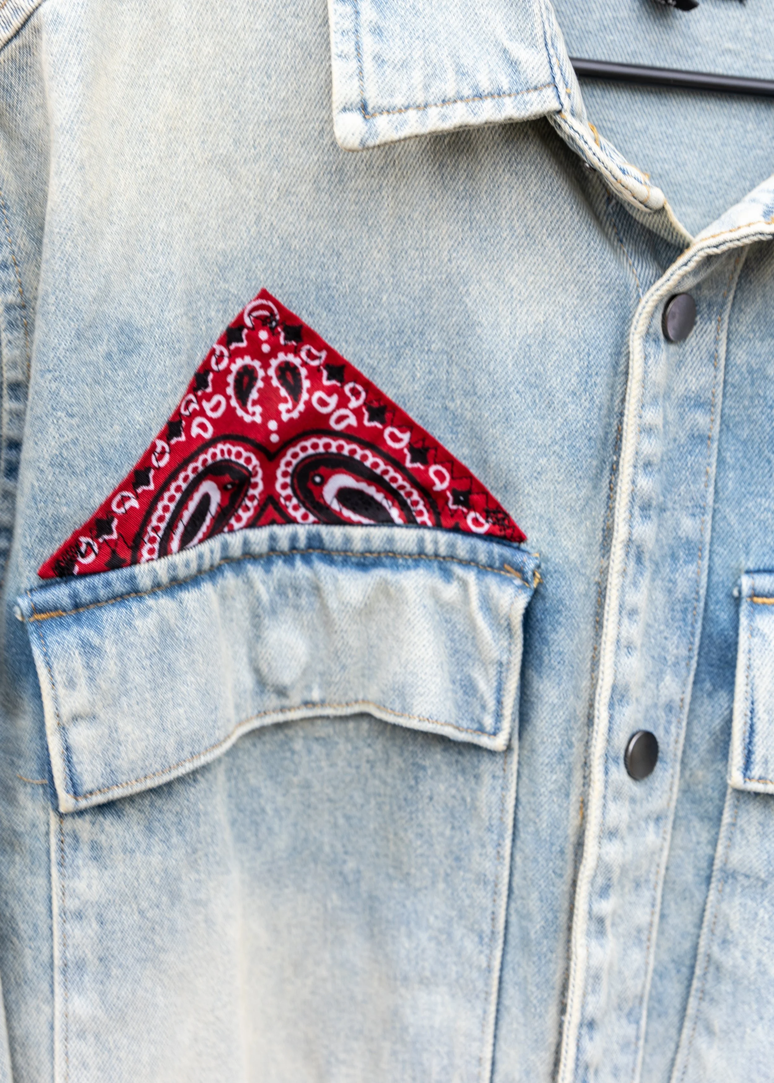 Close-up of a light blue denim jacket with a red and black bandana in the front pocket.