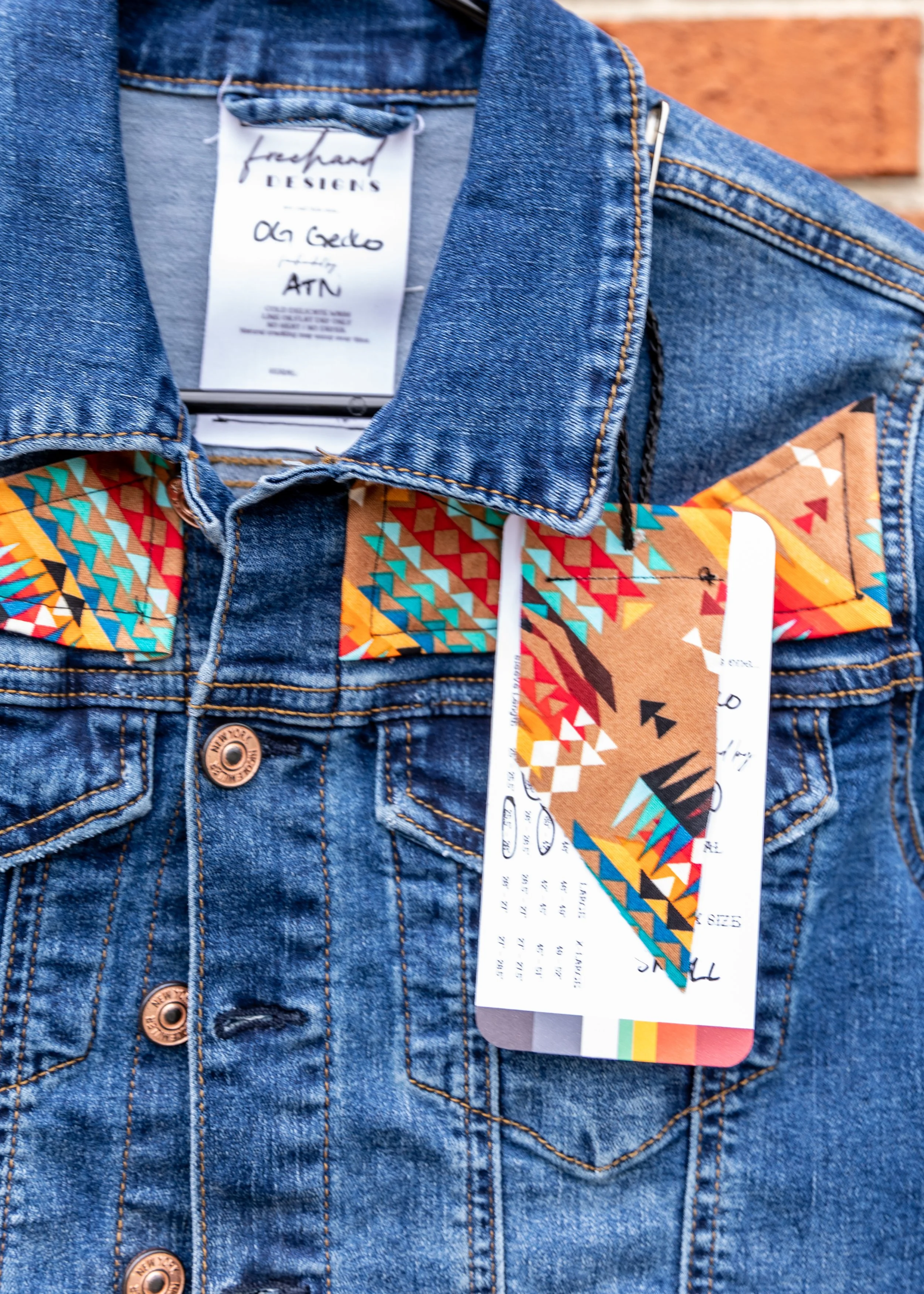 Close-up of a denim jacket with a colorful geometric-patterned collar and retail tags attached.