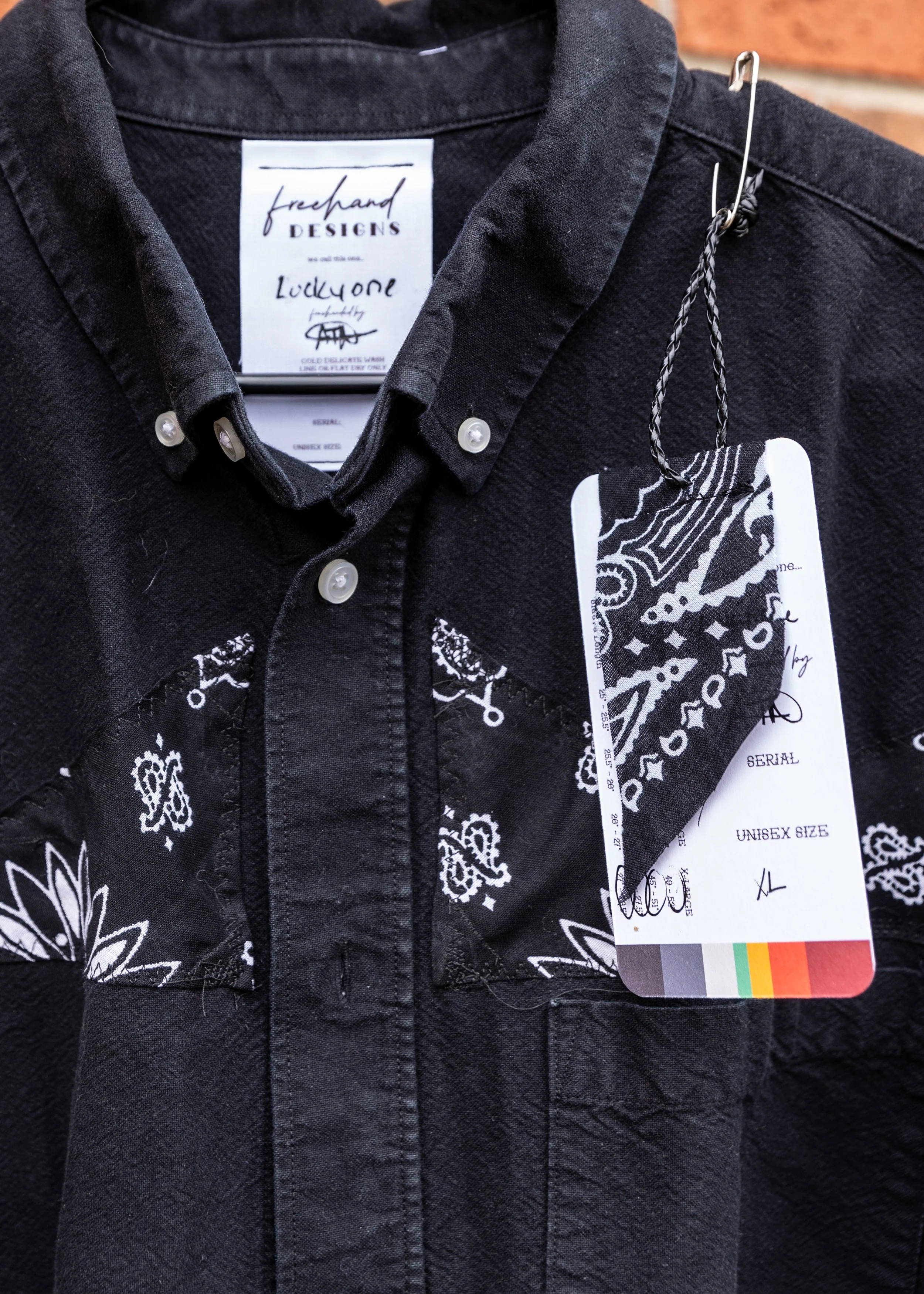 Close-up of a black shirt with white paisley pattern, still on a hanger, with tags attached showing size and brand details.