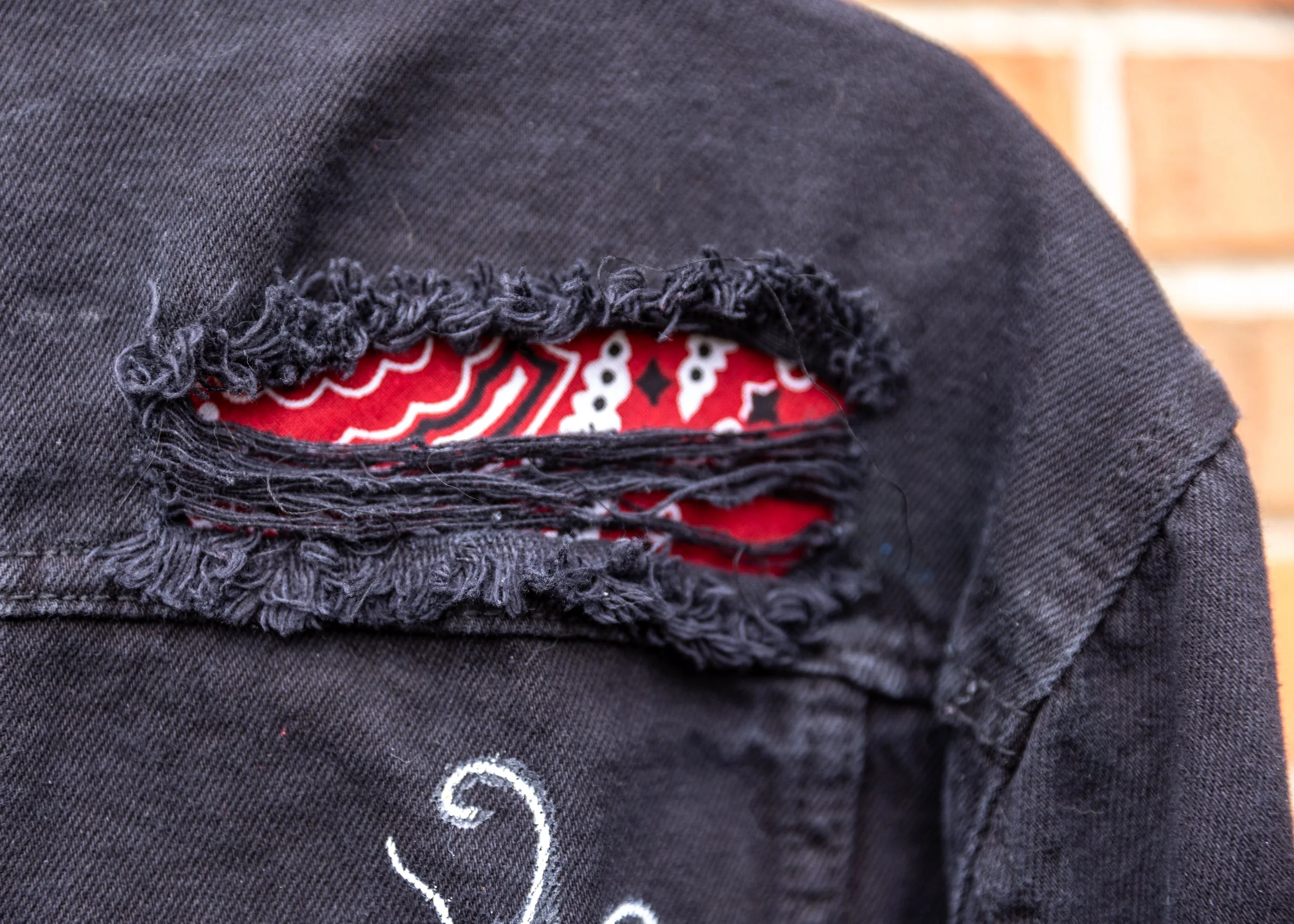 Close-up photo of torn black jeans with frayed edges, revealing red and white patterned fabric underneath.