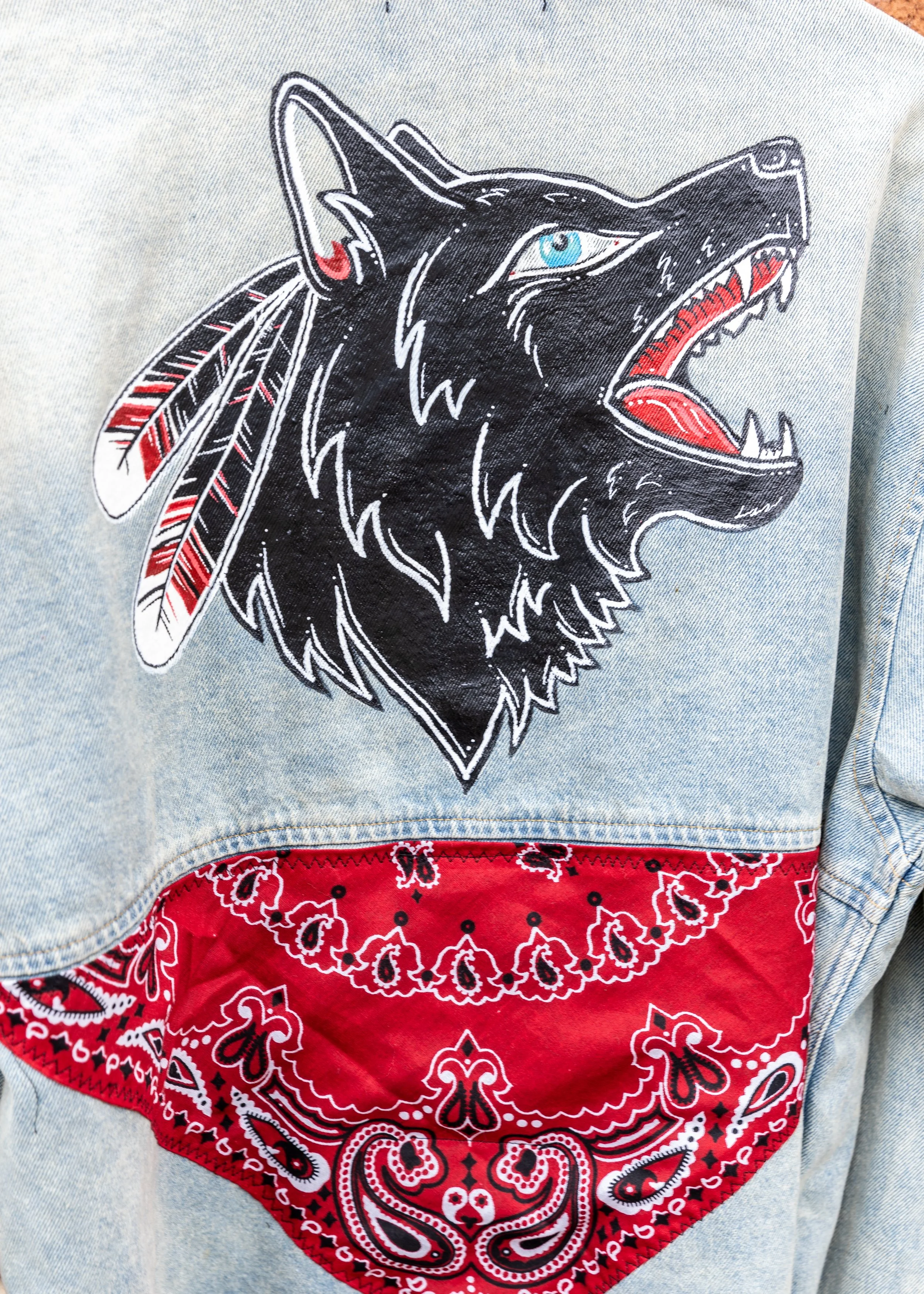Close-up of a piece of clothing with a large embroidered wolf head patch on the chest, a red bandana pattern on the bottom, and part of a light blue denim jacket.