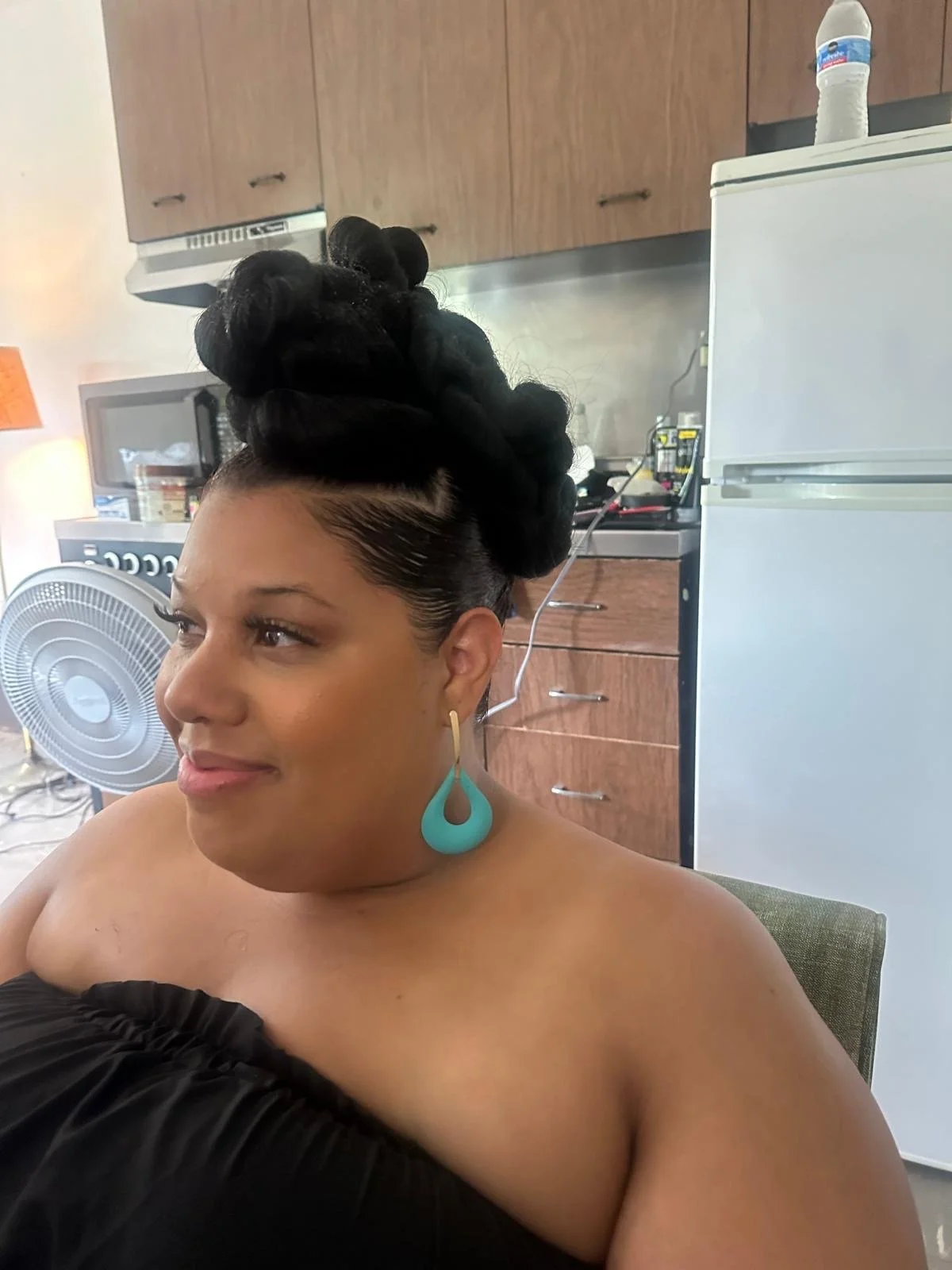 A woman with a large black hairstyle and turquoise earrings sitting in a kitchen.
