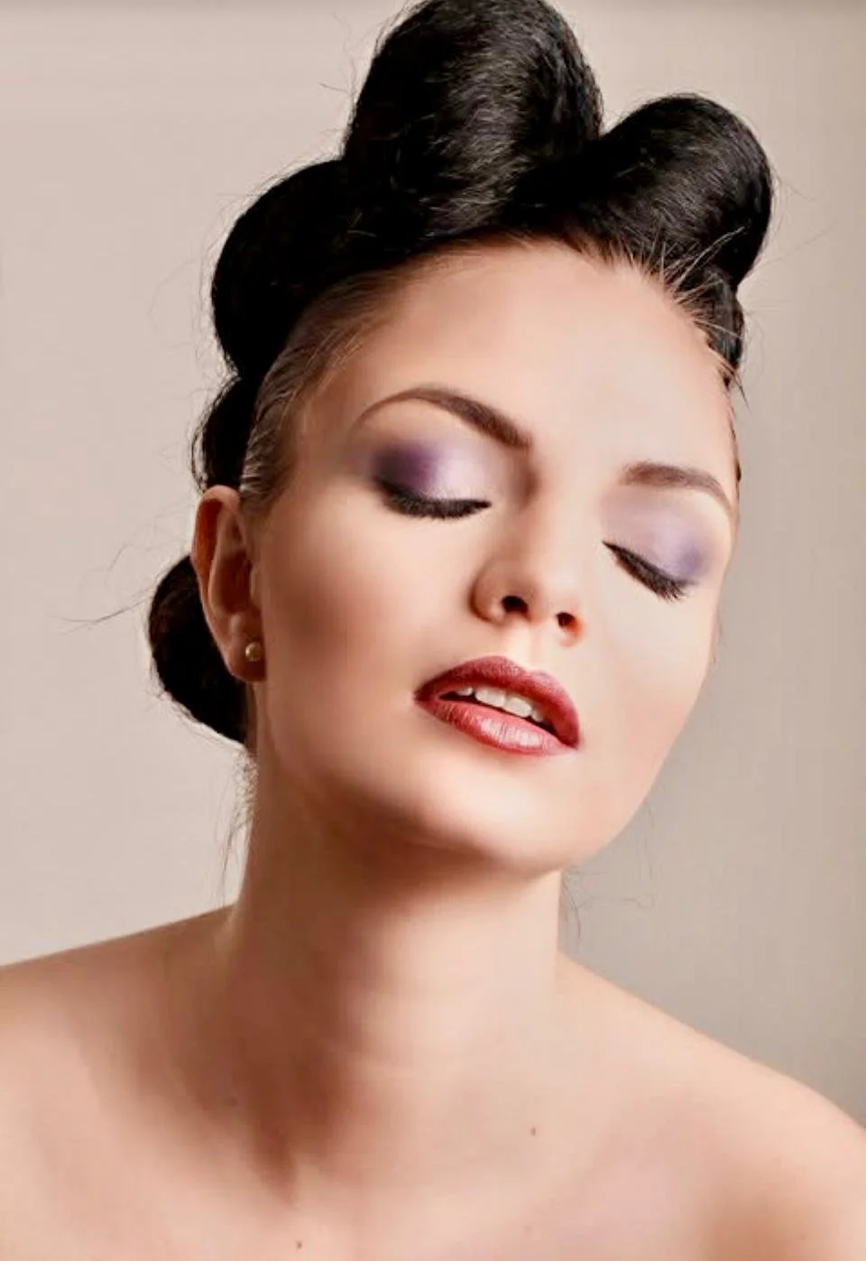 Portrait of a woman with vintage hairstyle, purple eye makeup, and red lipstick.