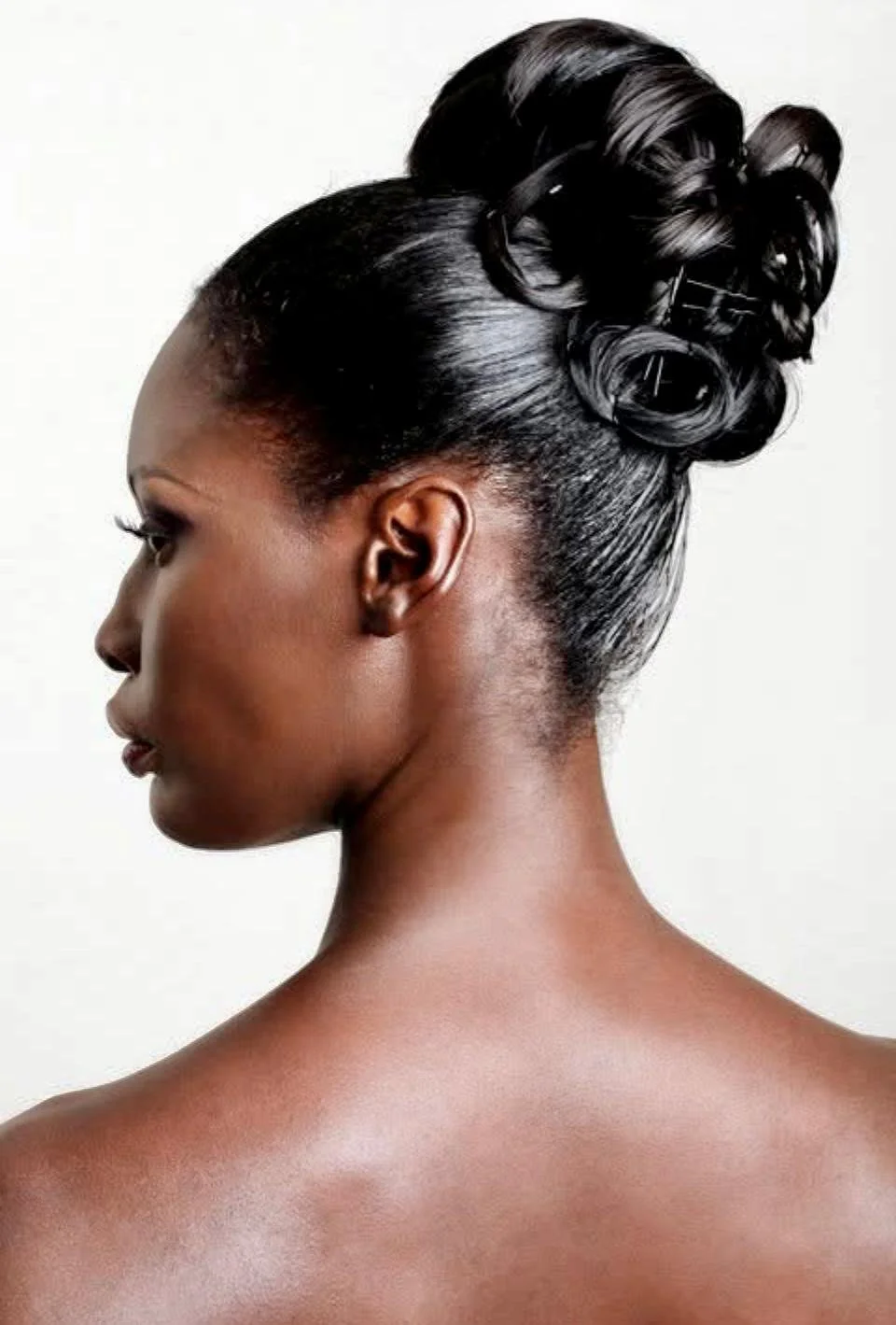 Side profile of a woman with dark skin and elegant black hair styled in intricate curled updo.