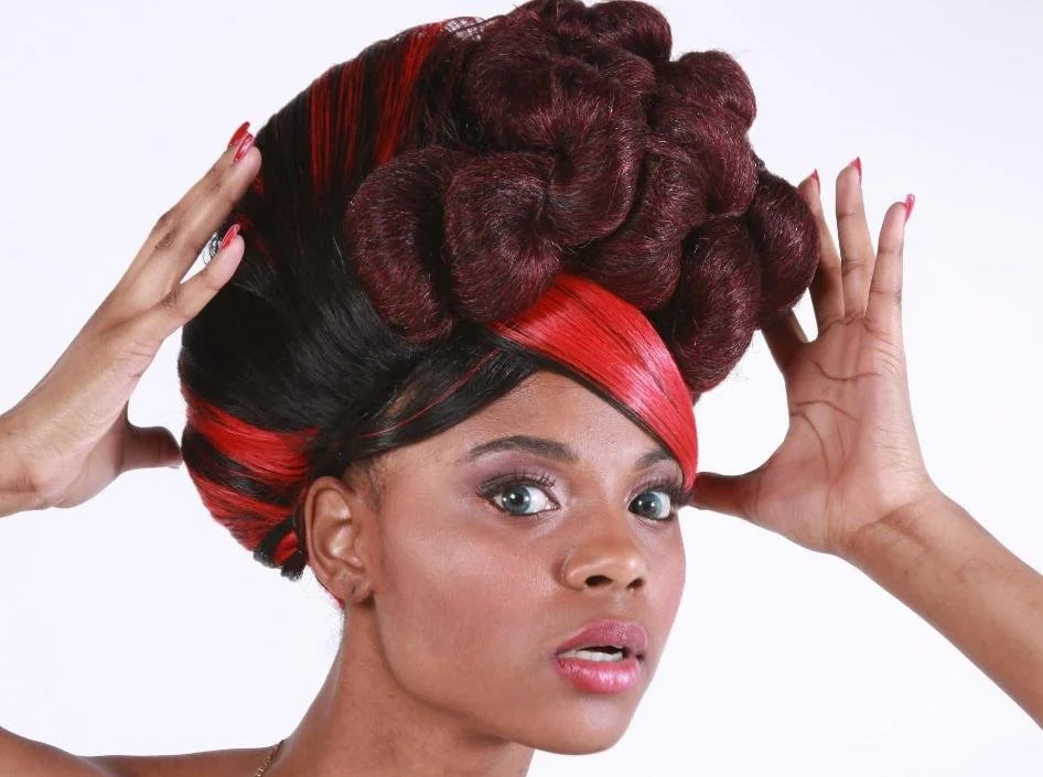 Woman with elaborate hairstyle featuring large, dark red and black hair buns and an asymmetrical red and black hair pattern.