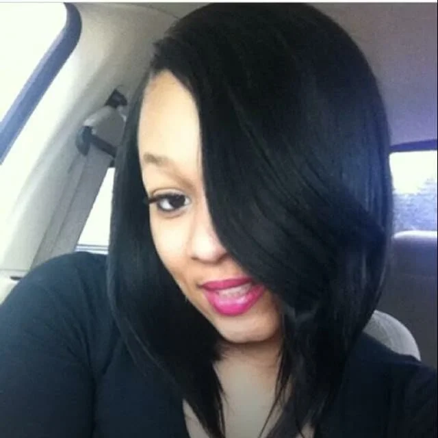 A woman with shoulder-length black hair, wearing pink lipstick, sitting inside a vehicle.