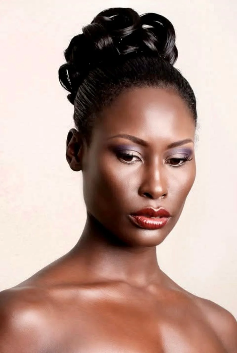 A portrait of a woman with dark skin, styled hair in an updo, subtle makeup, and a natural expression.