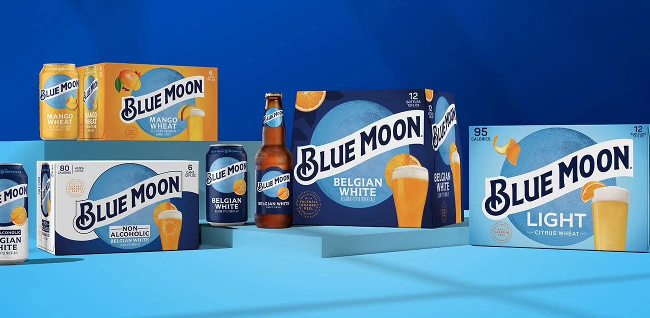 Various Blue Moon beer products, including cans and bottles, with packaging and branded boxes on a blue background.