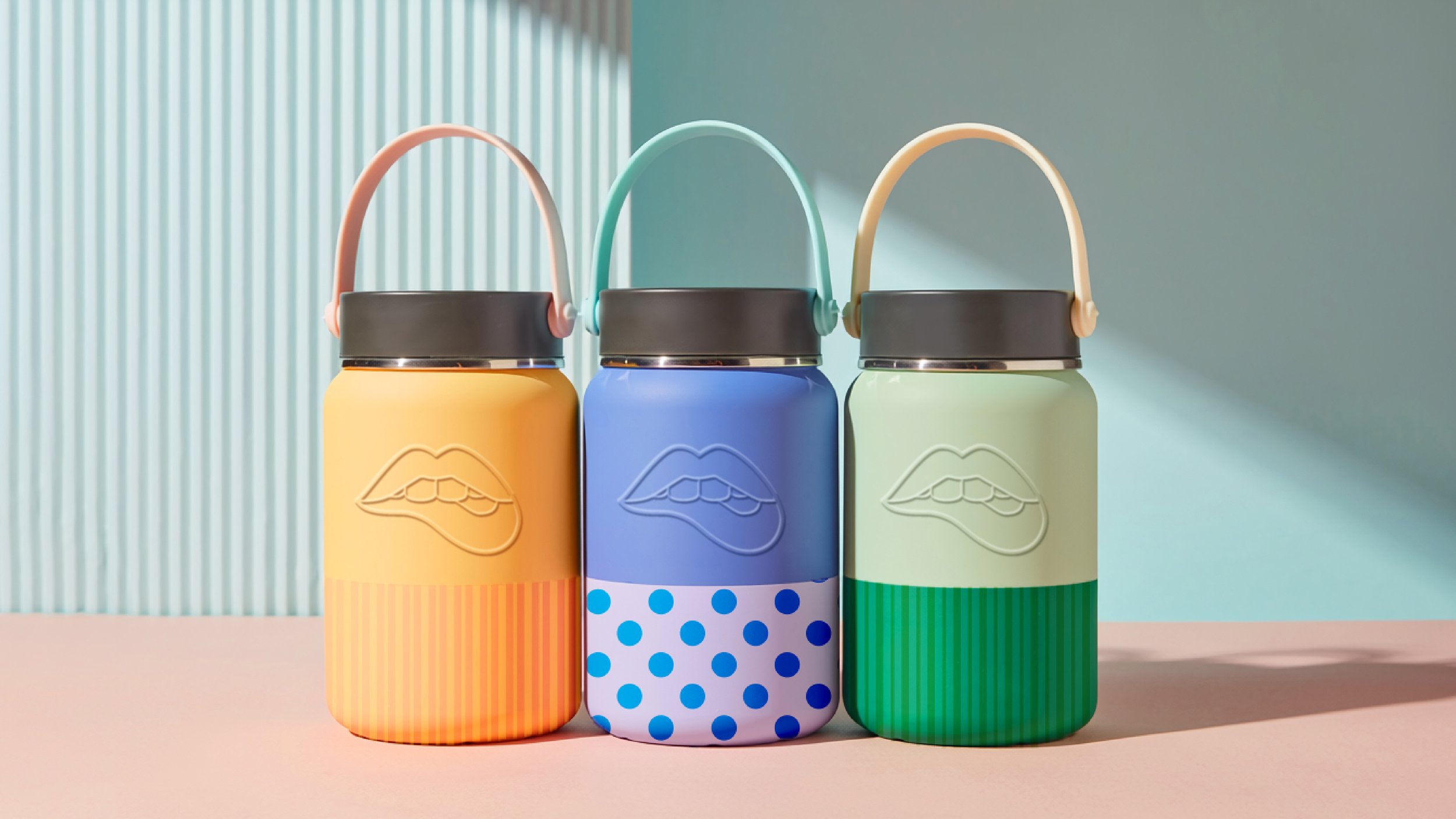 Three pastel-colored thermoses with lips embossed on their surfaces, arranged in a row against a light background with textured vertical lines.
