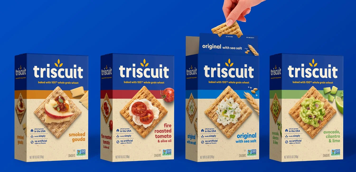 Four boxes of Triscuit crackers arranged in a row against a blue background, with a hand placing a cracker with sea salt flavor into one of the boxes.