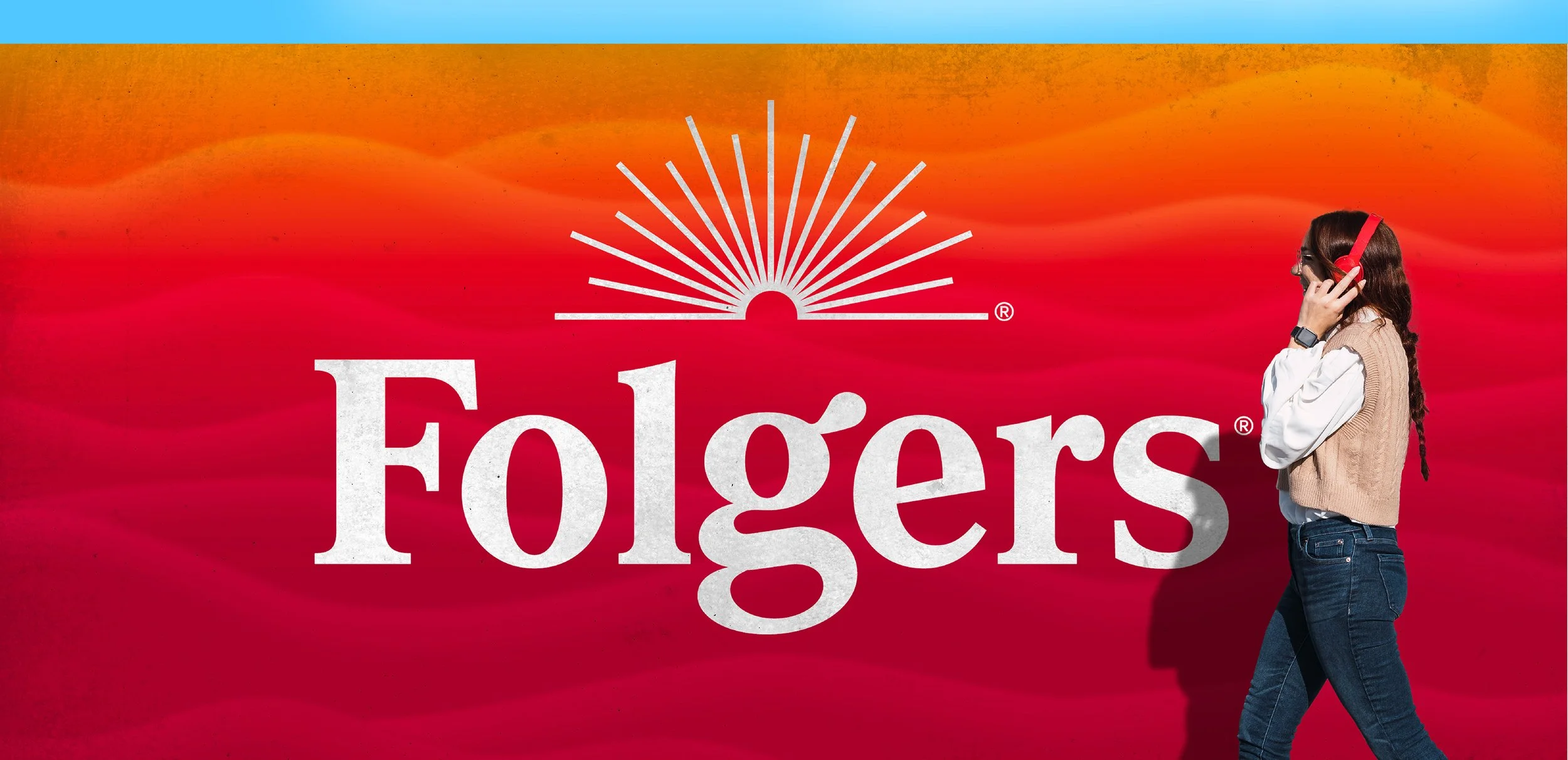 A large sign with a red and orange sunset background displays the word 'Foliage' in white letters. A woman with long dark hair, wearing a beige vest, white shirt, jeans, and red headphones, is walking past the sign.