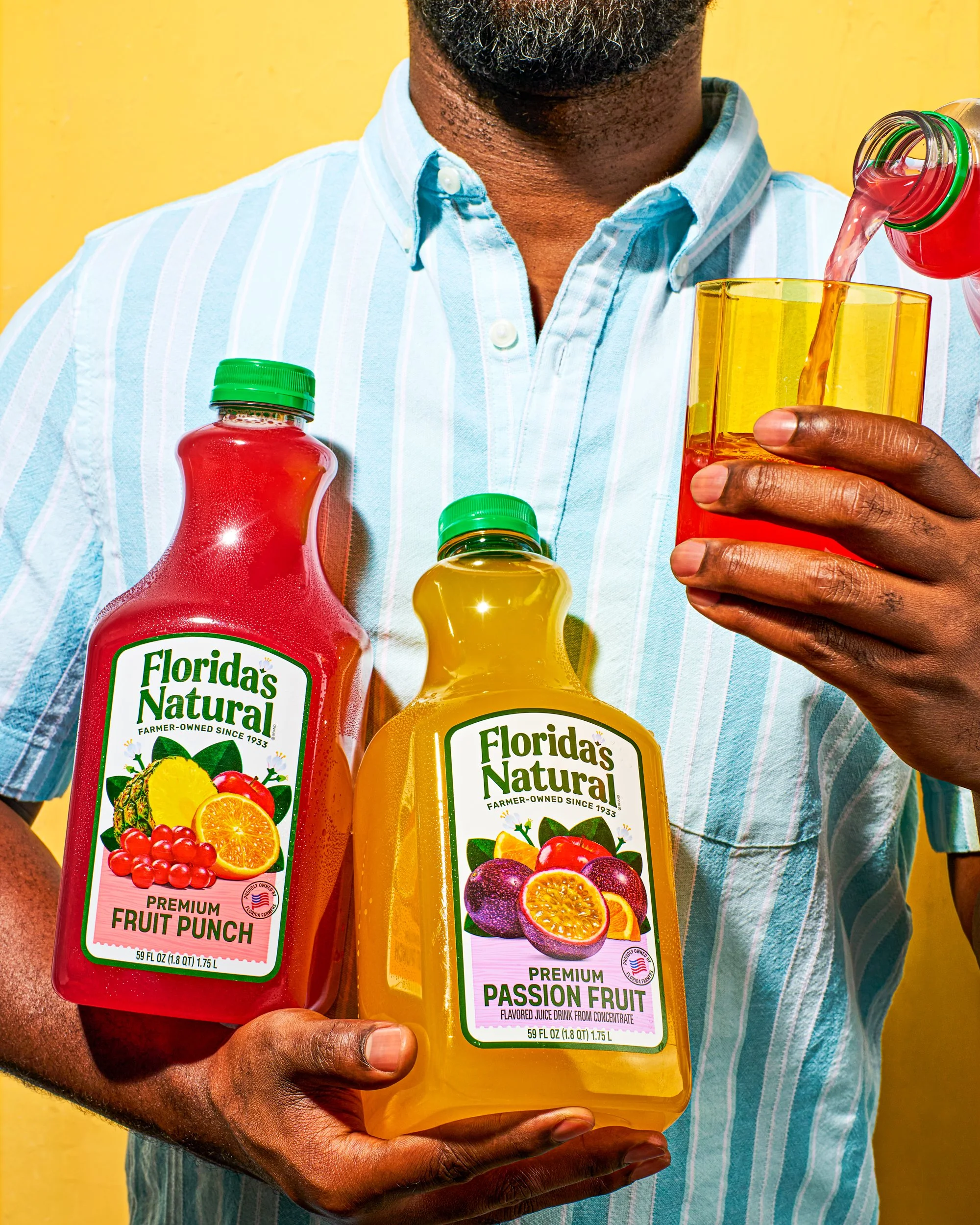 A person holding two bottles of Florida's Natural fruit juice, one labeled 'Premium Fruit Punch' and the other 'Premium Passion Fruit', with a yellow background.