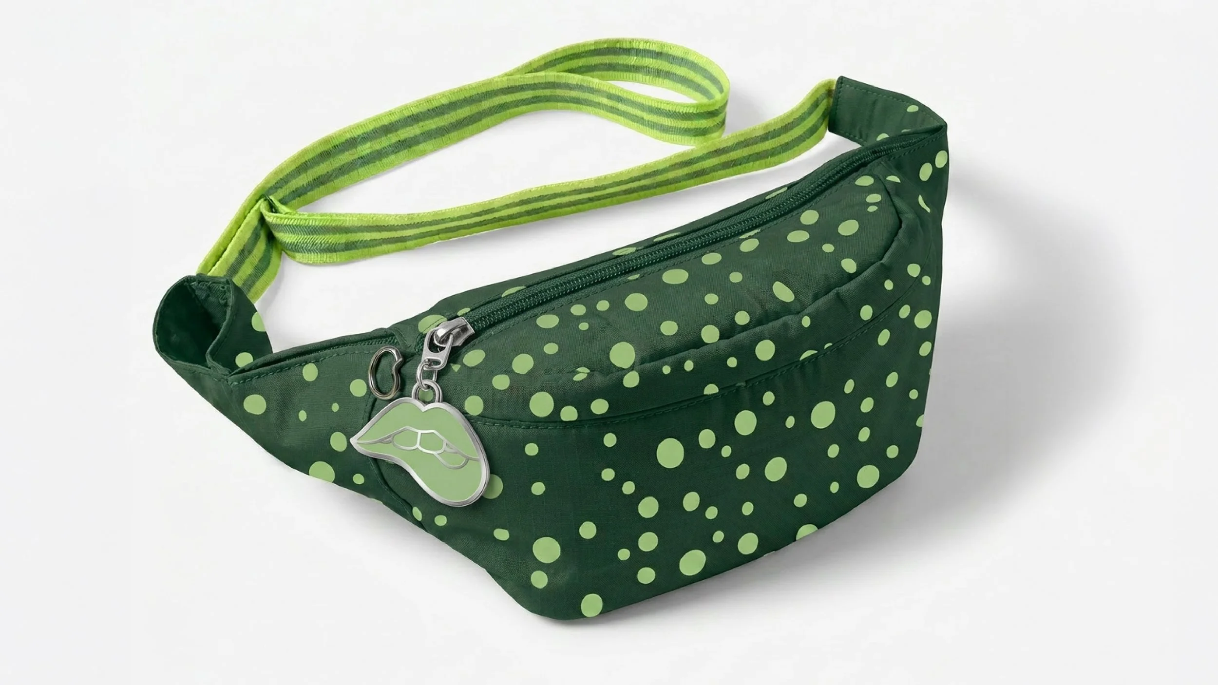 Green polka dot fanny pack with a zippered compartment and a green and striped strap, decorated with a lip-shaped charm.