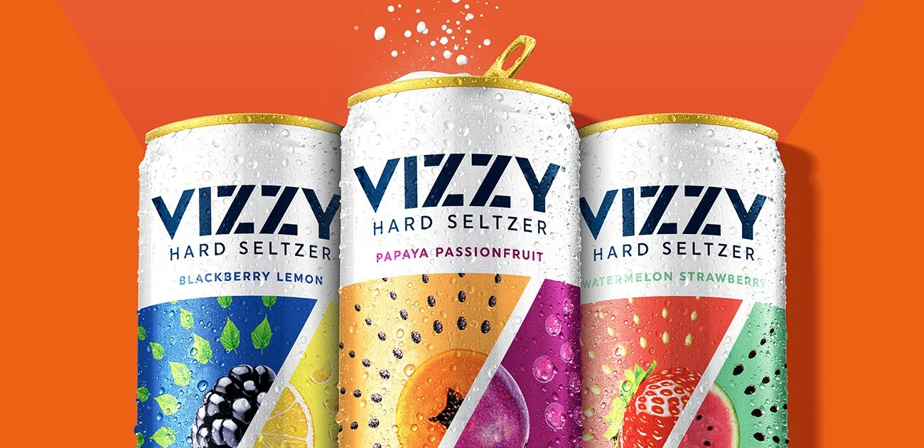 Three Vizzy hard seltzer cans, package design by Soulsight, on an orange background, featuring flavors Blackberry Lemon, Papaya Passionfruit, and Watermelon Strawberry, with droplets of condensation on the cans.
