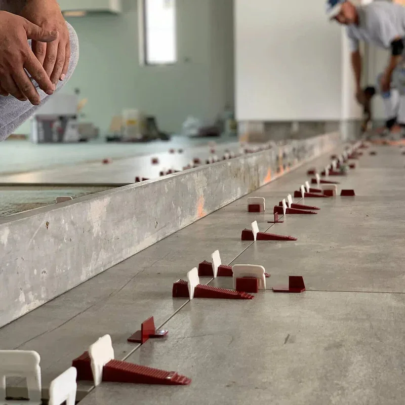 Close-up of red and white tile leveling spacers and wedges used for leveling tiles during installation, with workers in the background.