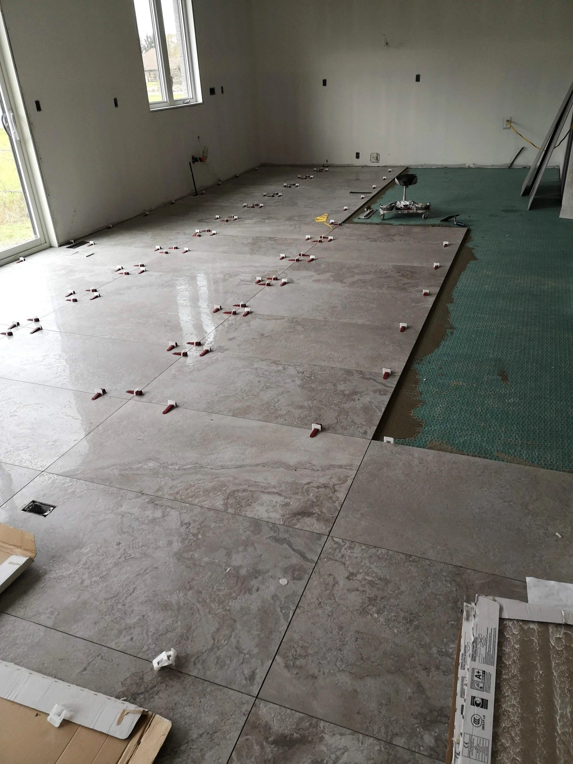 Room with new tile flooring being installed, with tiles partially laid and spacers in place, outside natural light coming through windows.