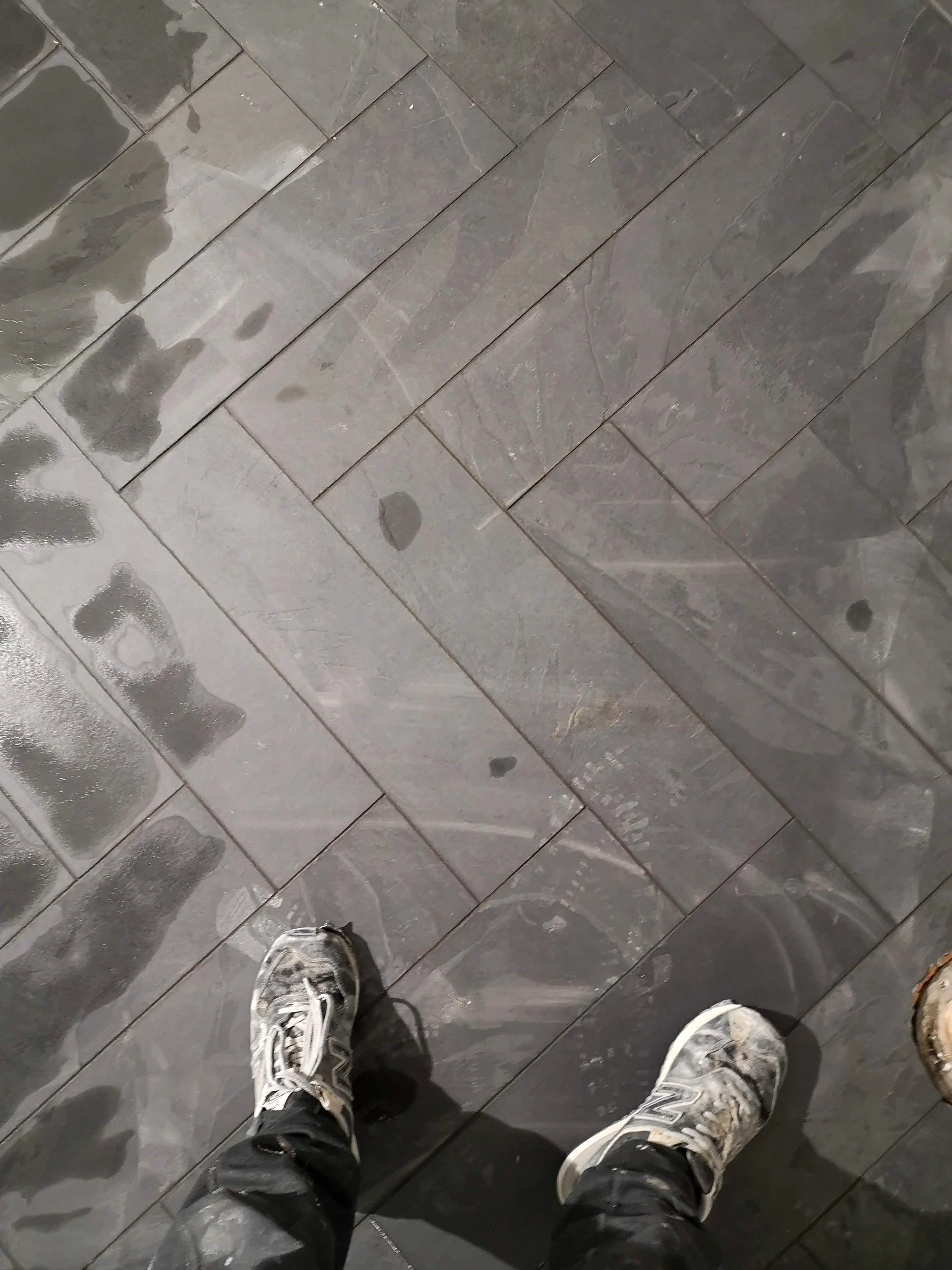 View of a tiled floor with two muddy sneakers and part of a person's legs visible.