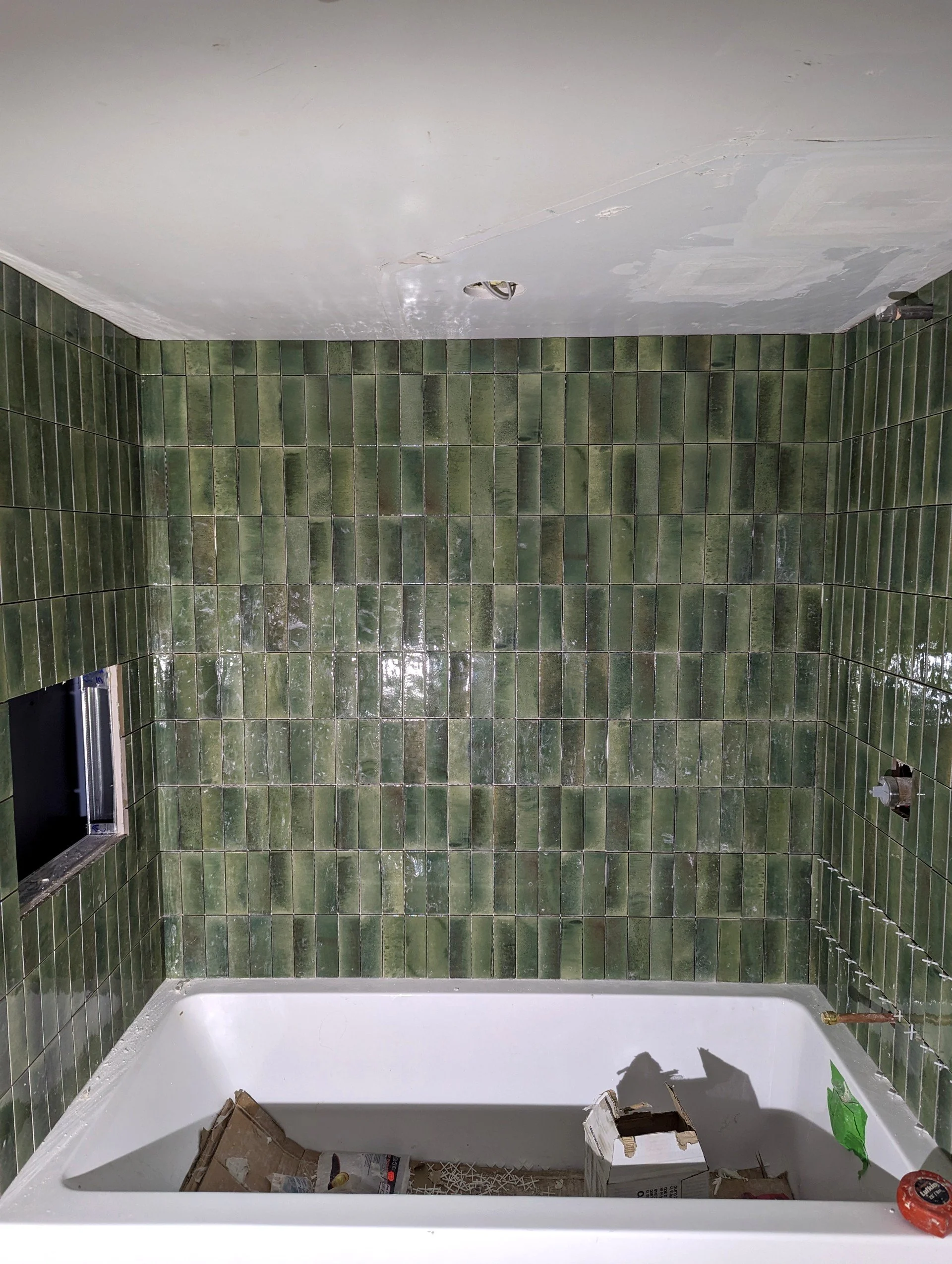 Green tiled bathroom with a bathtub and various renovation tools and materials inside.
