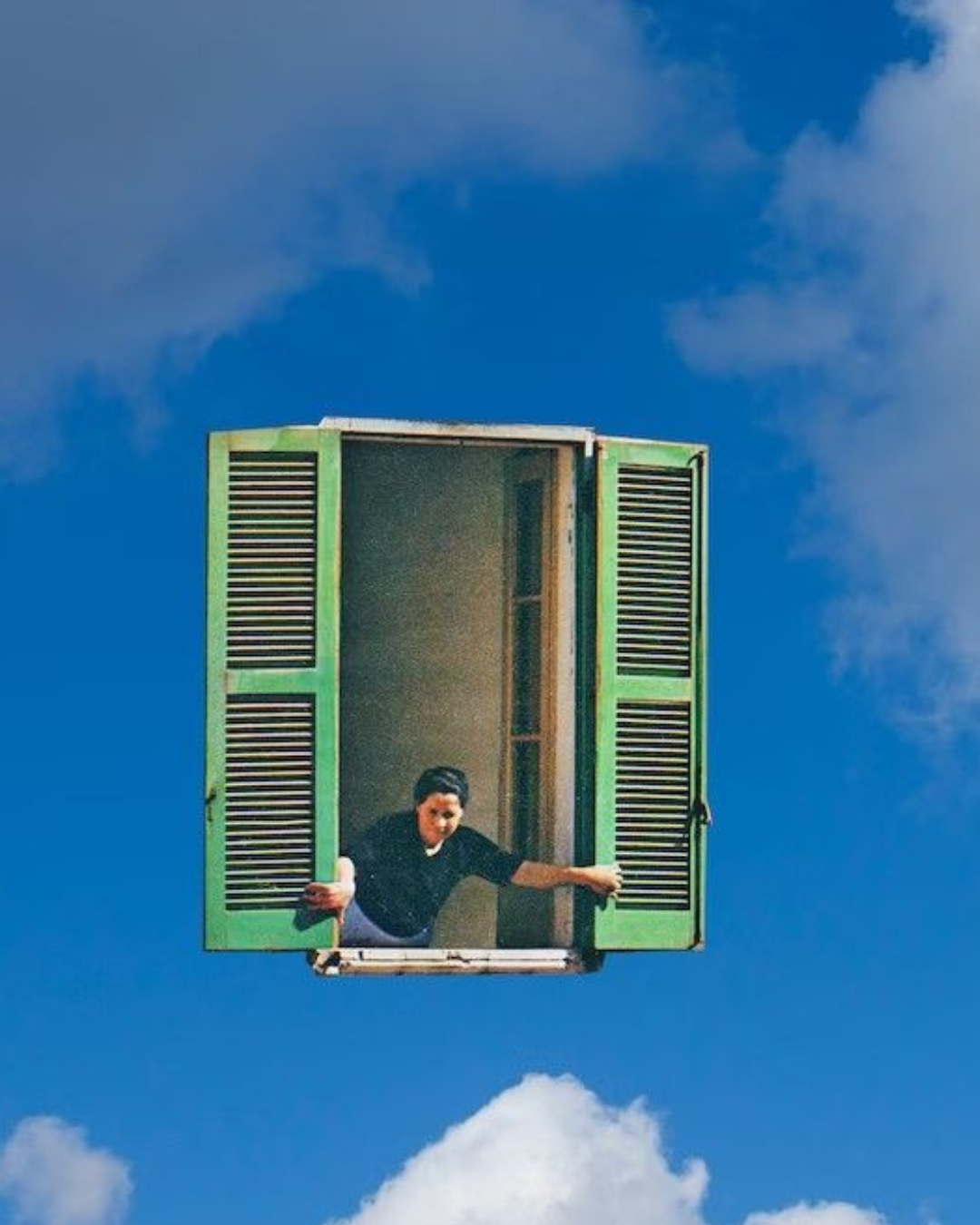 A person leaning out of open window with green shutters, appearing to float in the sky among clouds.