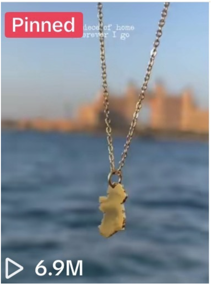 A necklace with a yellow pendant shaped like the state of New York, hanging over a body of water with a city skyline in the background.