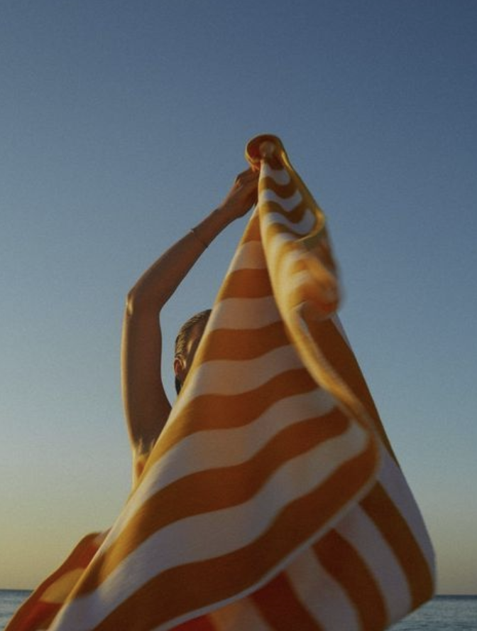 Person holding an orange and white striped fabric or towel against a blue sky background.