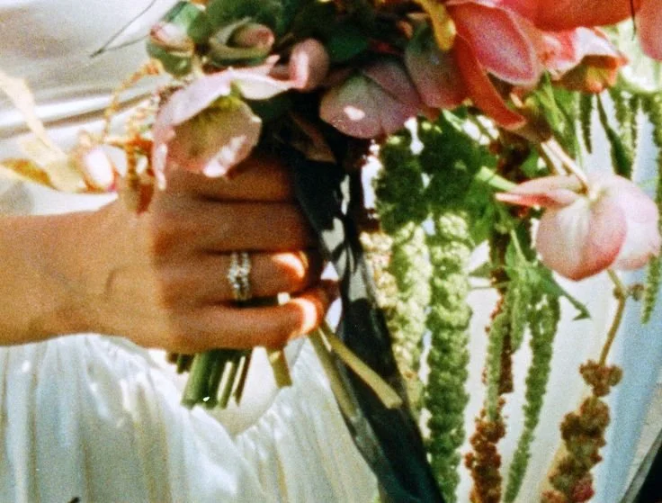 Close-up of a hand holding a colorful bouquet of flowers with pink, green, and purple blooms and greenery.
