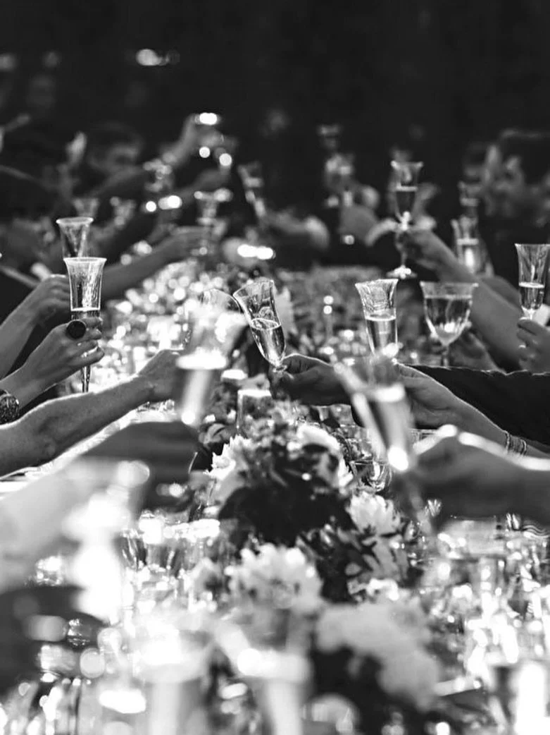 People at a celebration raising champagne flutes in a toast across a decorated table.