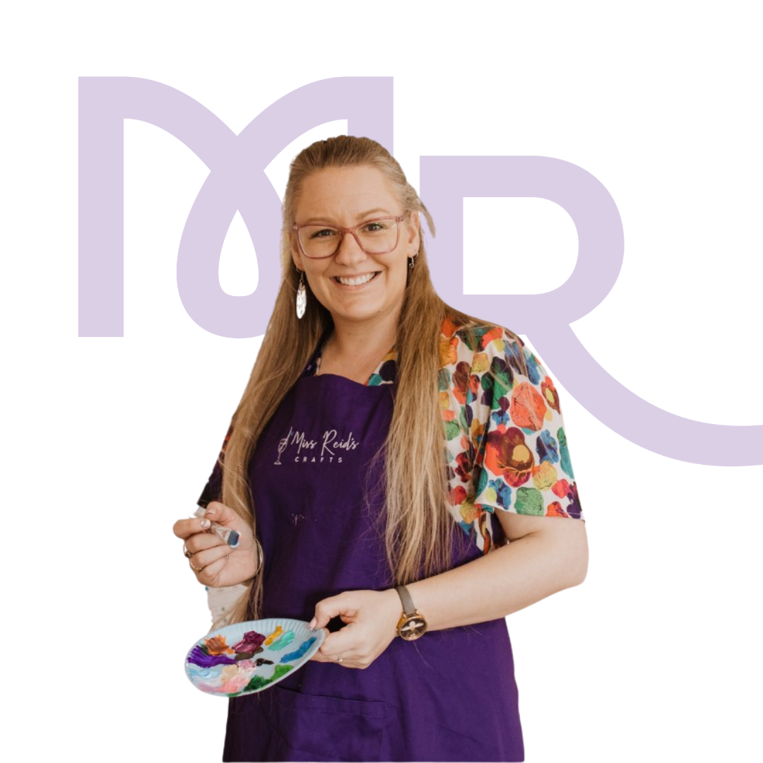 A woman with long blonde hair and glasses holding a paint palette, wearing a colorful floral shirt and a purple apron that says Miss Reid's Crafts, smiling in front of a white background with purple text.