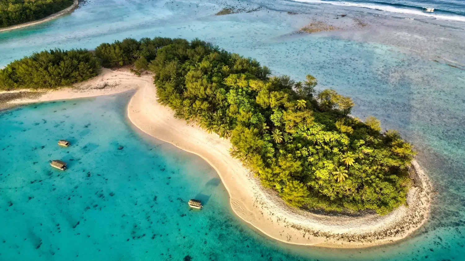 An aerial view of a lush, green island surrounded by clear, turquoise water with four boats anchored nearby.