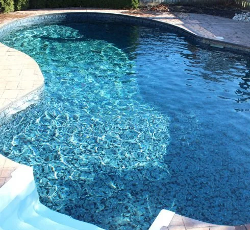A swimming pool with blue water and a curved edge, surrounding a paved deck area.