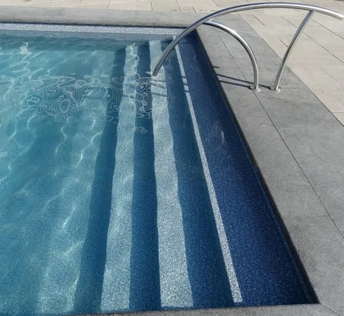 Close-up of a swimming pool with stainless steel handrail and tiled steps.