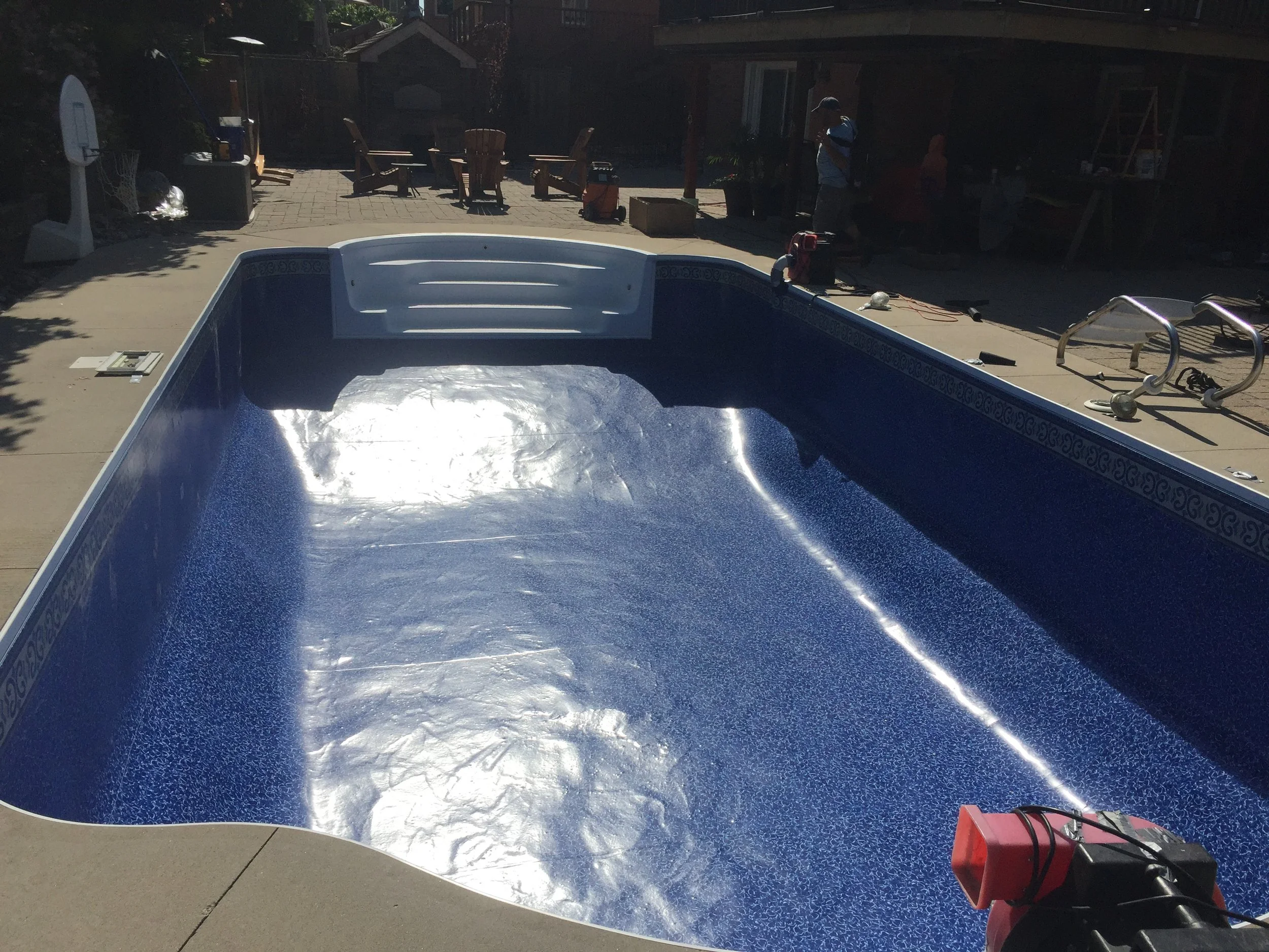Empty residential swimming pool being filled with water, located in a backyard patio area.