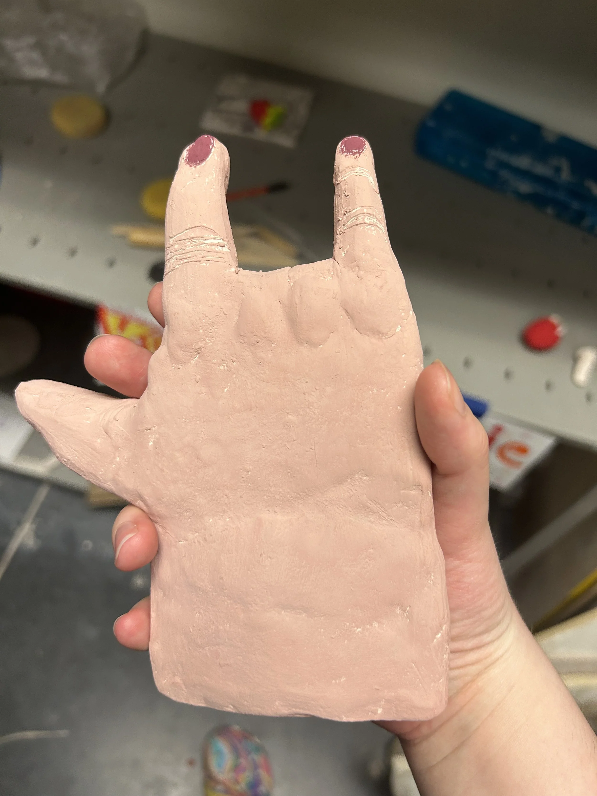 A person holding a ceramic sculpture of a hand making the 'I love you' gesture with the index and pinky fingers raised.