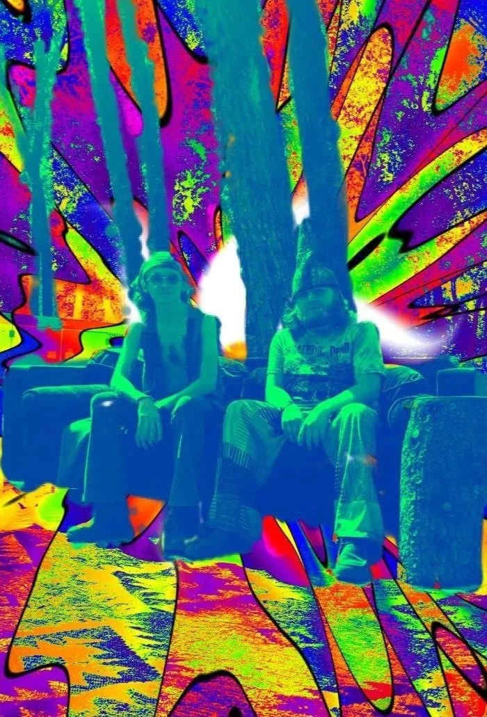 The founders of the band, Andrew Locke and Jackie Dwayne, pose sitting down in front of a tie-dye background