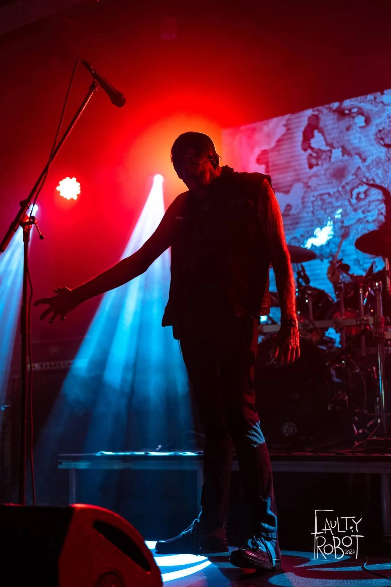 Silhouette of a person on stage with colorful stage lights and a backdrop showing an artistic blue and white scene.