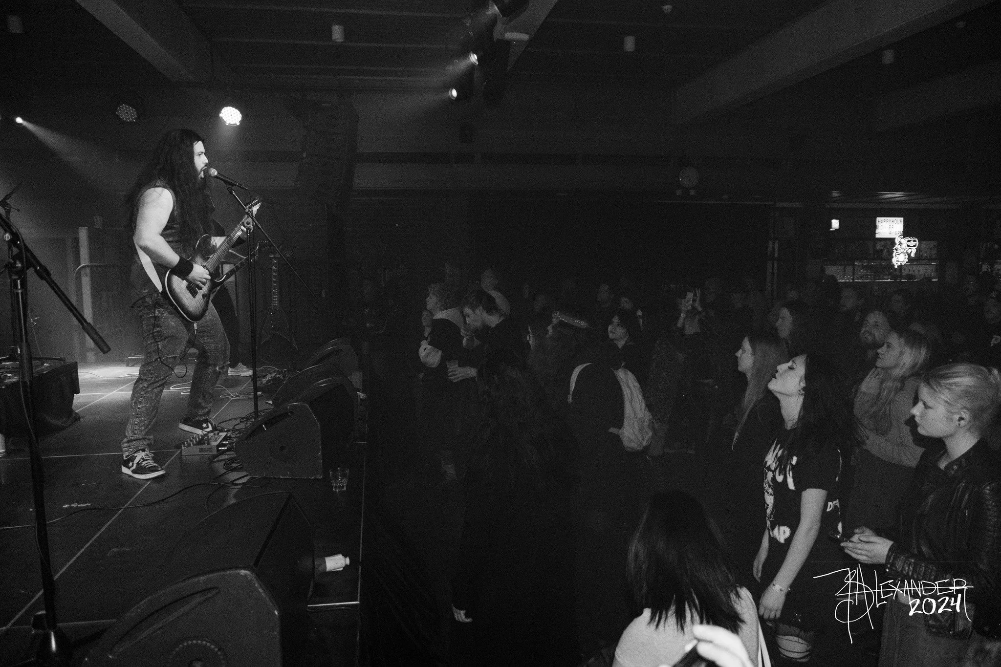 A black and white photo of a live music concert with a guitarist on stage and an audience watching.