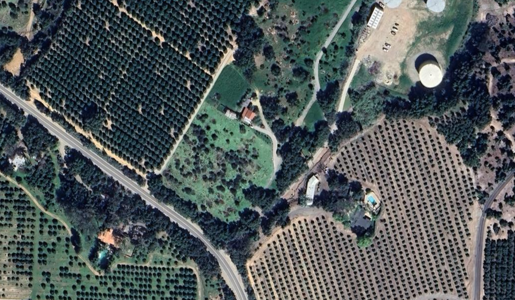 Aerial view of a rural area with fields, orchards, trees, a house, and a swimming pool of Maricopa Gardens back in 1950s.