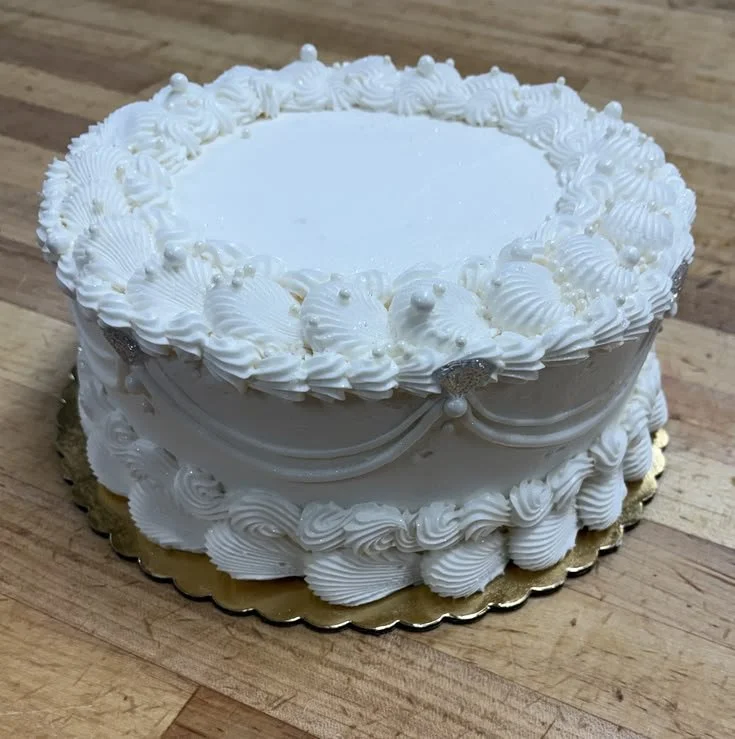A white decorated cake with fluffy icing and pearl-like accents, on a wooden surface.